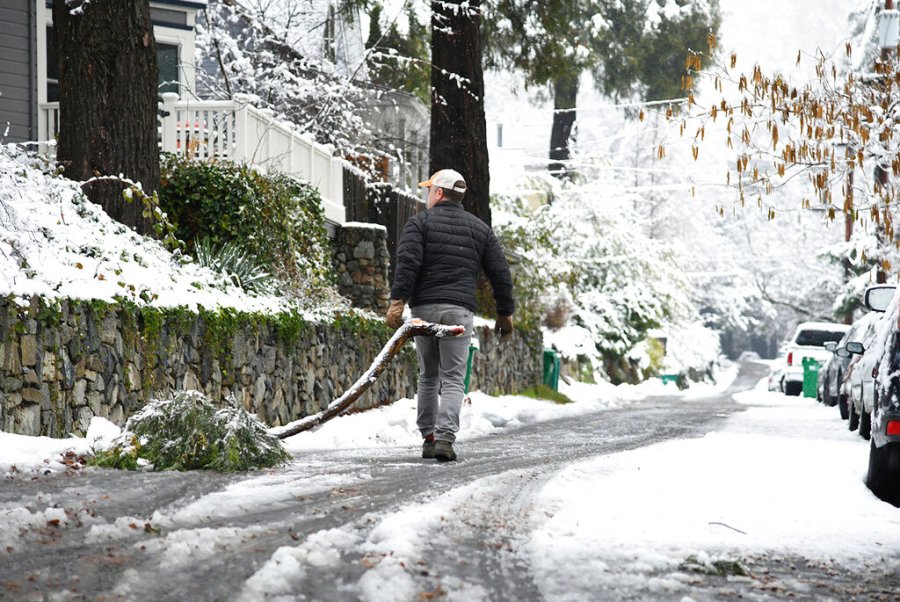 A resident removes a downed branch along Grove Street following a snow and rain storm, early Tuesday, Dec. 14, 2021, in Nevada City, Calif. (Elias Funez/The Union via AP)