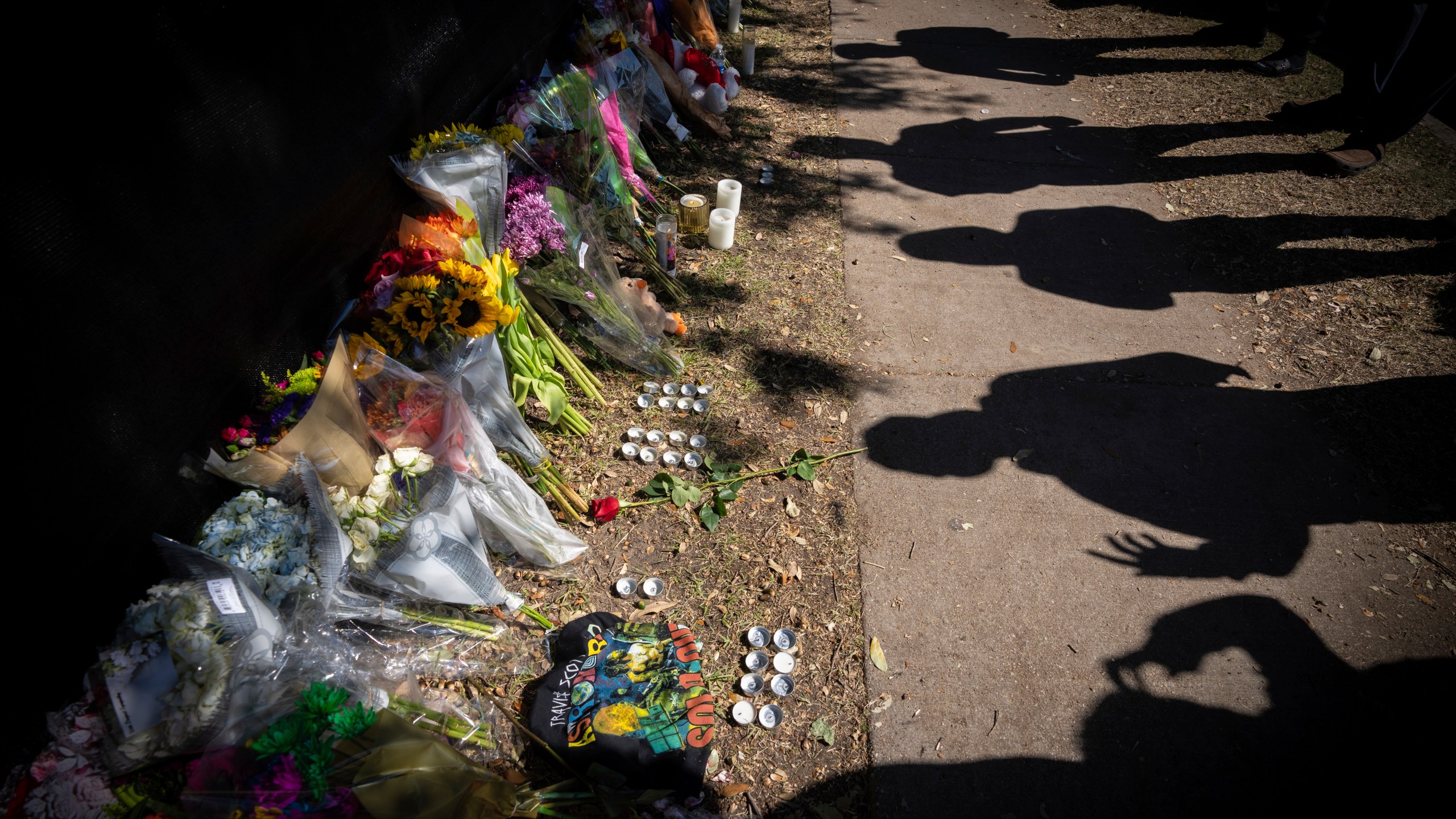 Visitors cast shadows at a memorial to the victims of the Astroworld concert in Houston on Nov. 7, 2021. The 10 people who lost their lives in a massive crowd surge at the Astroworld music festival in Houston died from compression asphyxia, officials announced Thursday, Dec. 16, 2021. (AP Photo/Robert Bumsted, File)