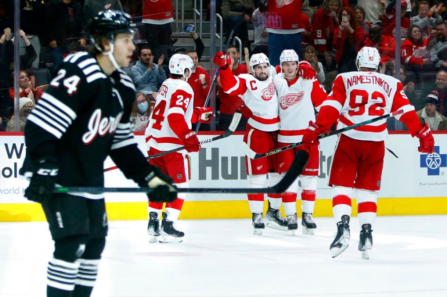 Detroit Red Wings center Dylan Larkin, third from left, celebrates his second goal of the game with center Pius Suter (24), defenseman Gustav Lindstrom and center Vladislav Namestnikov (92) as New Jersey Devils defenseman Ty Smith (24) skates off during the second period of an NHL hockey game Saturday, Dec. 18, 2021, in Detroit. (AP Photo/Duane Burleson)