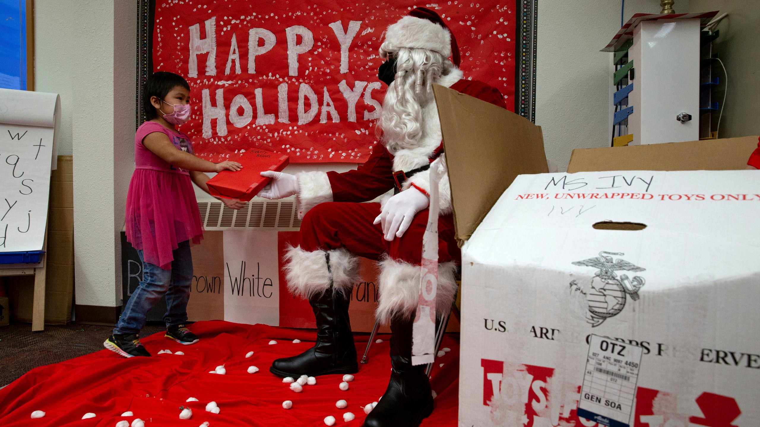 In a photo provided by the U.S. Marine Corps, U.S. Marine Corps Staff Sgt. Federico Gomez, dressed as Santa Claus, hands a gift to a student in Shungnak, Alaska, Dec. 8, 2021. Marines on snowmobiles delivered toys to boys and girls in Alaska's Arctic. (Cpl. Brendan Mullin/U.S. Marine Corps via AP )