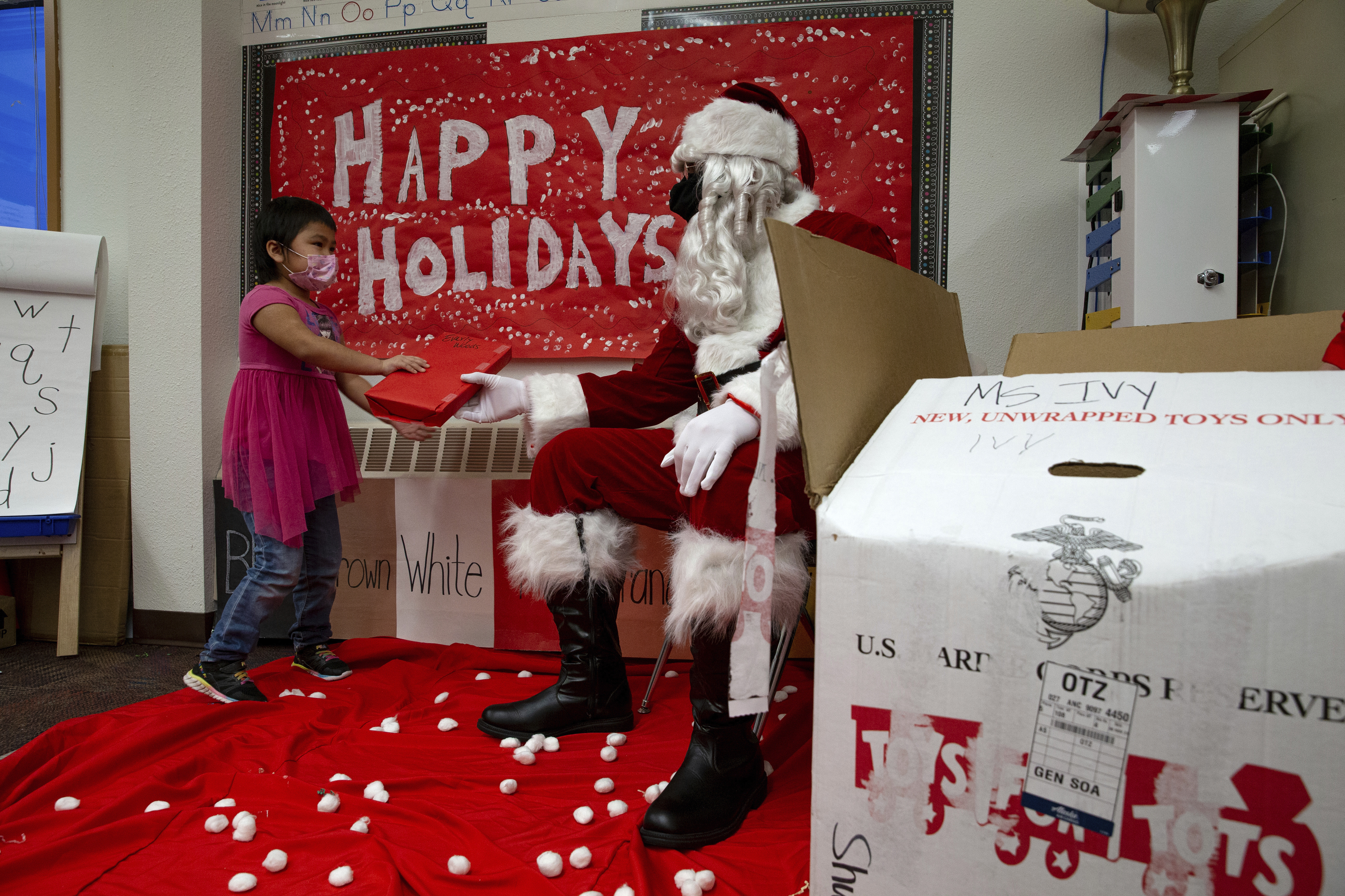 In a photo provided by the U.S. Marine Corps, U.S. Marine Corps Staff Sgt. Federico Gomez, dressed as Santa Claus, hands a gift to a student in Shungnak, Alaska, Dec. 8, 2021. Marines on snowmobiles delivered toys to boys and girls in Alaska's Arctic. (Cpl. Brendan Mullin/U.S. Marine Corps via AP )