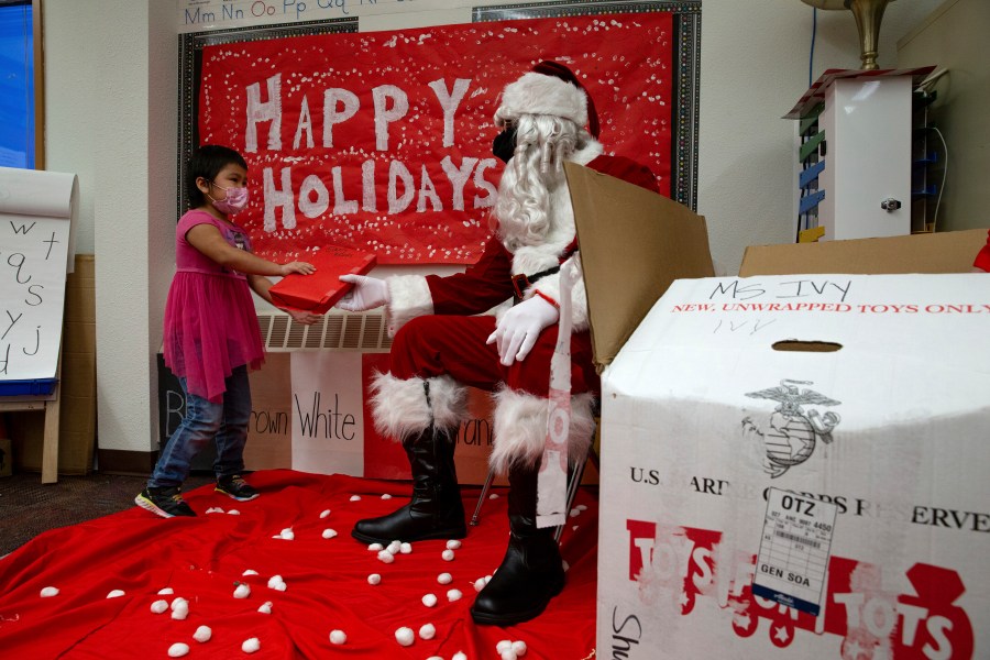 In a photo provided by the U.S. Marine Corps, U.S. Marine Corps Staff Sgt. Federico Gomez, dressed as Santa Claus, hands a gift to a student in Shungnak, Alaska, Dec. 8, 2021. Marines on snowmobiles delivered toys to boys and girls in Alaska's Arctic. (Cpl. Brendan Mullin/U.S. Marine Corps via AP )