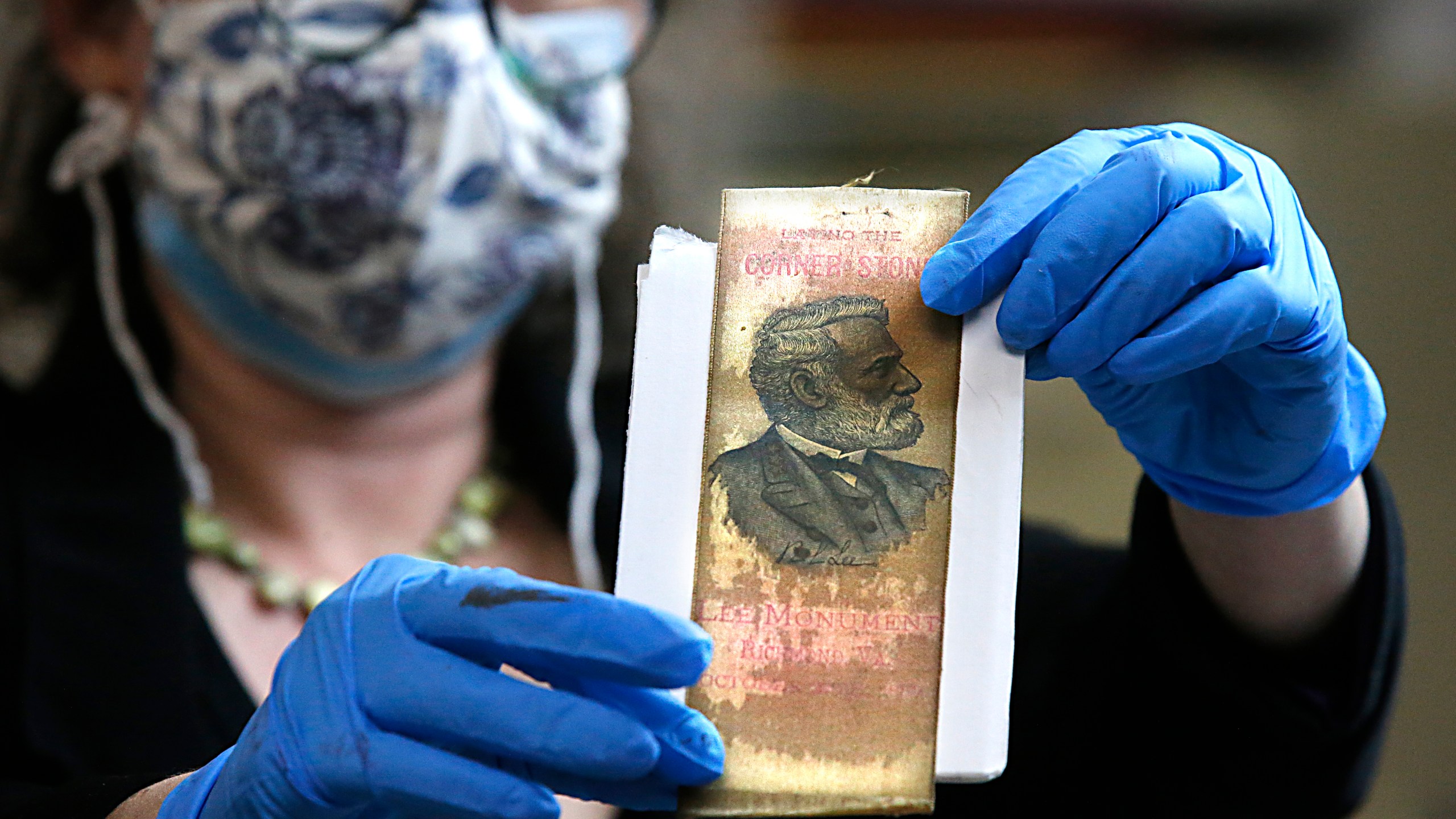 Gretchen Guidess holds up a ribbon with the likeness of Robert E. Lee, which was one of the artifacts inside the copper box time capsule recovered from the base of the Robert E. Lee monument, Tuesday, Dec. 28, 2021, at the Virginia Department of Historical Resources lab in Richmond, Va. (Bob Brown/Richmond Times-Dispatch via AP)