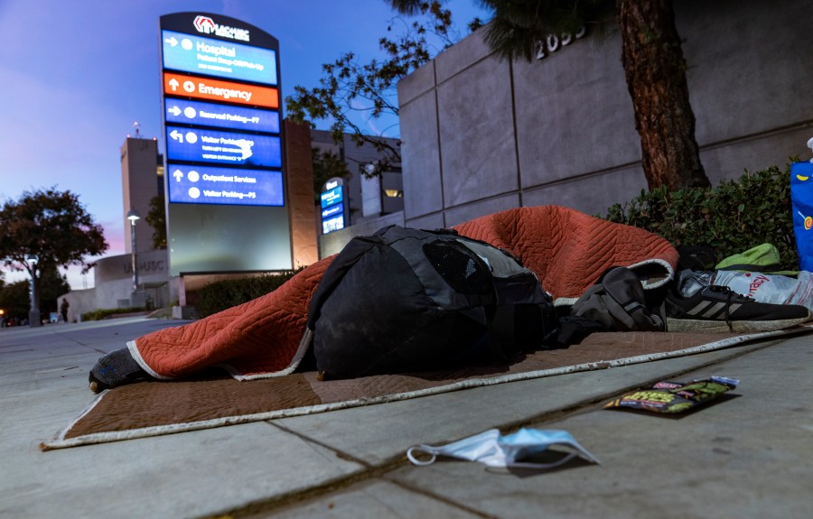 A homeless person sleeps outside the Los Angeles County+USC Medical Center entrance on Dec. 16, 2020. (AP Photo/Damian Dovarganes, File)