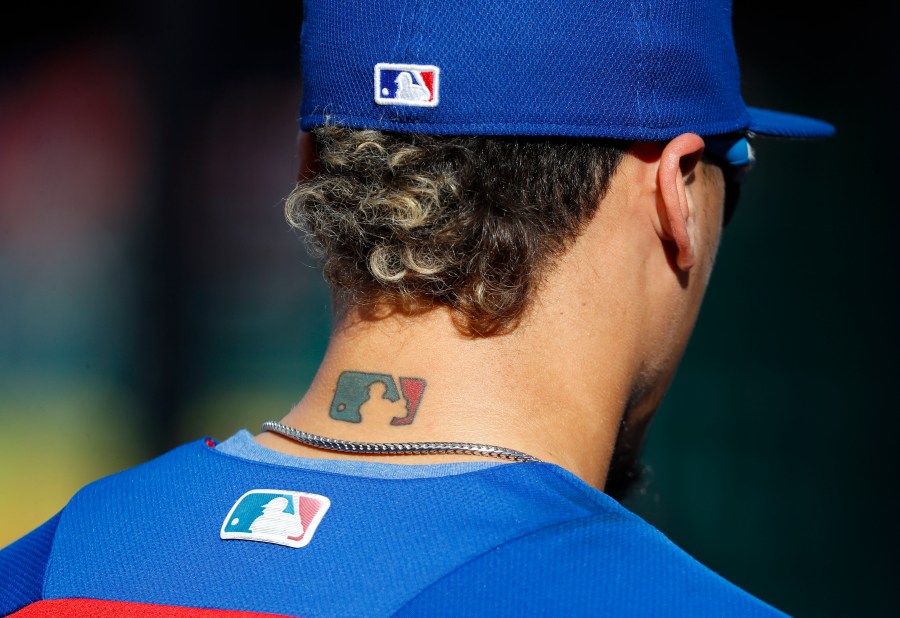 Then-Chicago Cubs' Javier Baez sports an MLB logo tattoo and logos on his hat and jersey as he waits to take batting practice before Game 2 of baseball's National League Division Series against the Washington Nationals at Nationals Park, Saturday, Oct. 7, 2017, in Washington. The clock ticked down toward the expiration of Major League Baseball’s collective bargaining agreement at 11:59 p.m. EST Wednesday night, Dec. 1, 2021, and what was likely to be a management lockout ending the sport’s labor peace at over 26 1/2 years. (AP Photo/Pablo Martinez Monsivais, File)