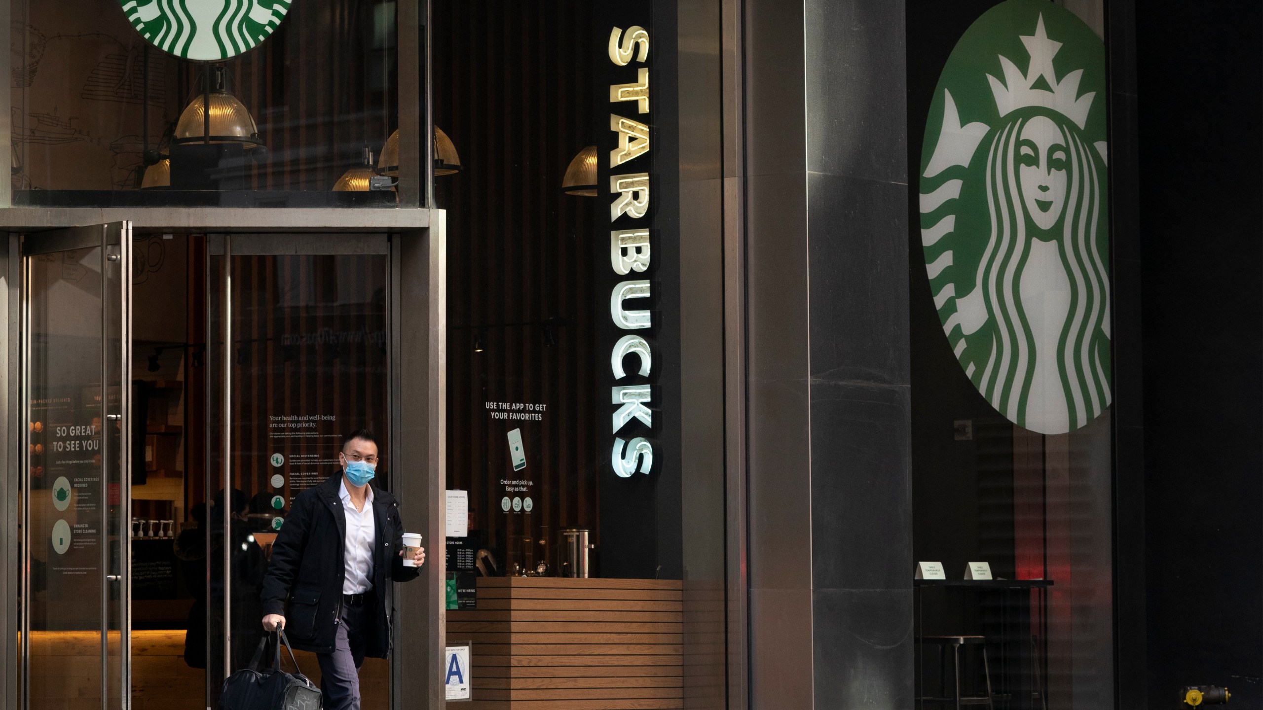 A man carries a beverage as he walks out of a Starbucks coffee shop, Tuesday, Jan. 19, 2021, in New York. (AP Photo/Mark Lennihan, File)