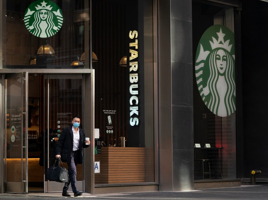 A man carries a beverage as he walks out of a Starbucks coffee shop, Tuesday, Jan. 19, 2021, in New York. (AP Photo/Mark Lennihan, File)