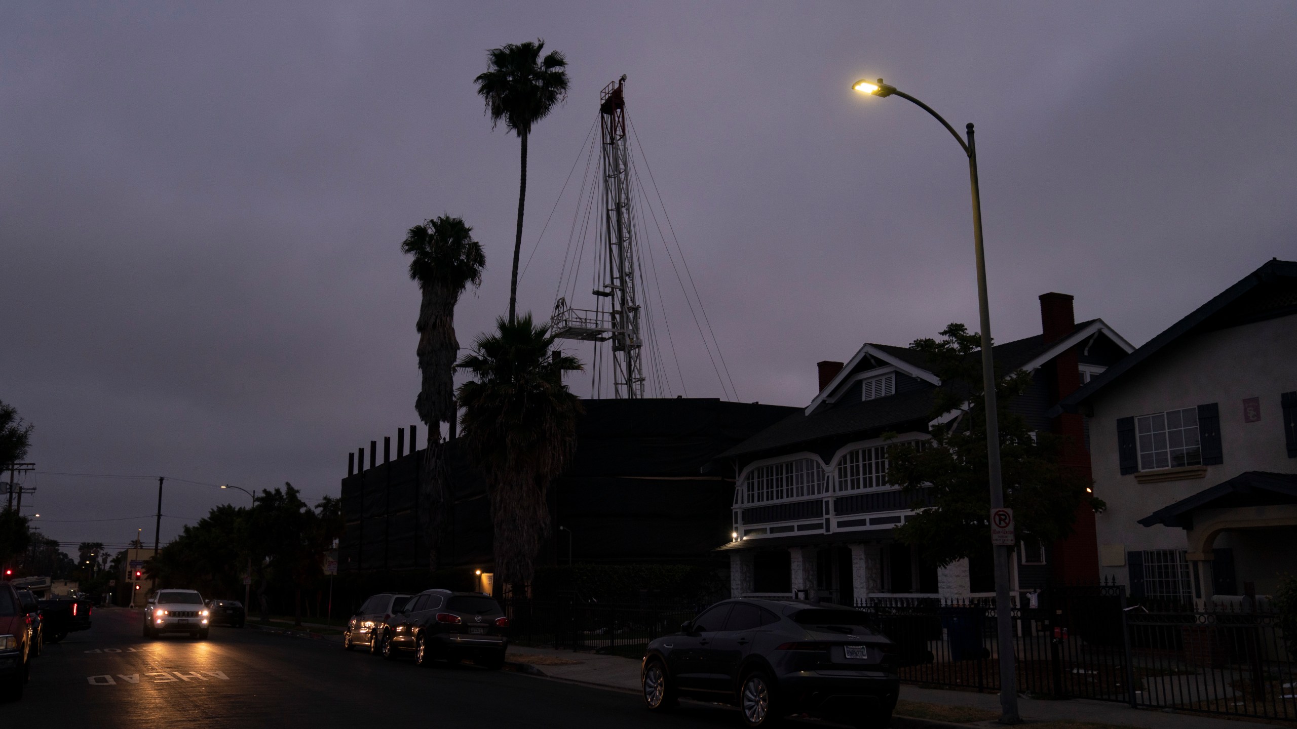 A vehicle drives past the Jefferson oil drill site located in the residential area in Los Angeles, Wednesday, June 2, 2021. University of Southern California researchers found people living near wells in Jefferson Park reported significantly higher rates of wheezing, eye and nose irritation, sore throat and dizziness than neighbors living farther away. The researchers likened the respiratory harm caused by living near the oil fields to daily exposure to secondhand smoke or exhaust from a busy highway. (AP Photo/Jae C. Hong)