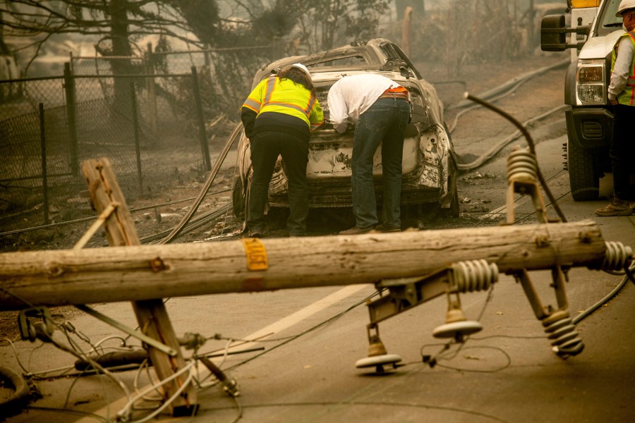 In this Nov. 10, 2018 file photo, with a downed power utility pole in the foreground, Eric England, right, searches through a friend's vehicle after the wildfire burned through Paradise, Calif. The nation's largest utility, Pacific Gas & Electric is poised to emerge from five years of criminal probation amid worries that it remains too dangerous to be trusted. Over the five years, the utility became an even more destructive force. More than 100 people have died and thousands of homes and businesses have been incinerated in wildfires sparked by its equipment in that time. (AP Photo/Noah Berger, File)