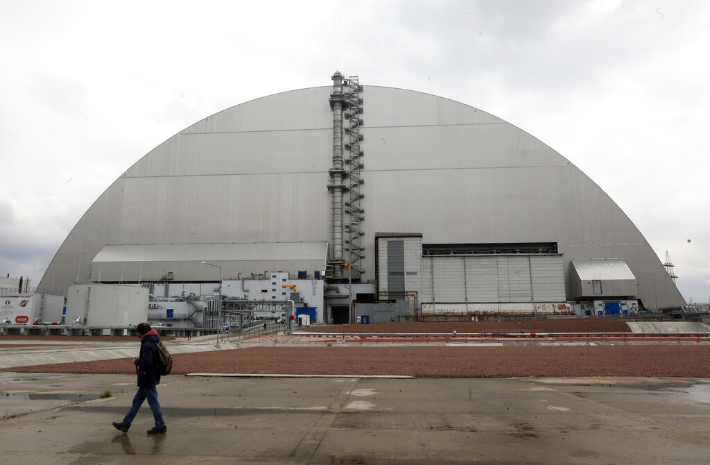 A man walks past a shelter covering the exploded reactor at the Chernobyl nuclear plant, in Chernobyl, Ukraine, Thursday, April 15, 2021. The vast and empty Chernobyl Exclusion Zone around the site of the world’s worst nuclear accident is a baleful monument to human mistakes. Yet 35 years after a power plant reactor exploded, Ukrainians also look to it for inspiration, solace and income. (AP Photo/Efrem Lukatsky)