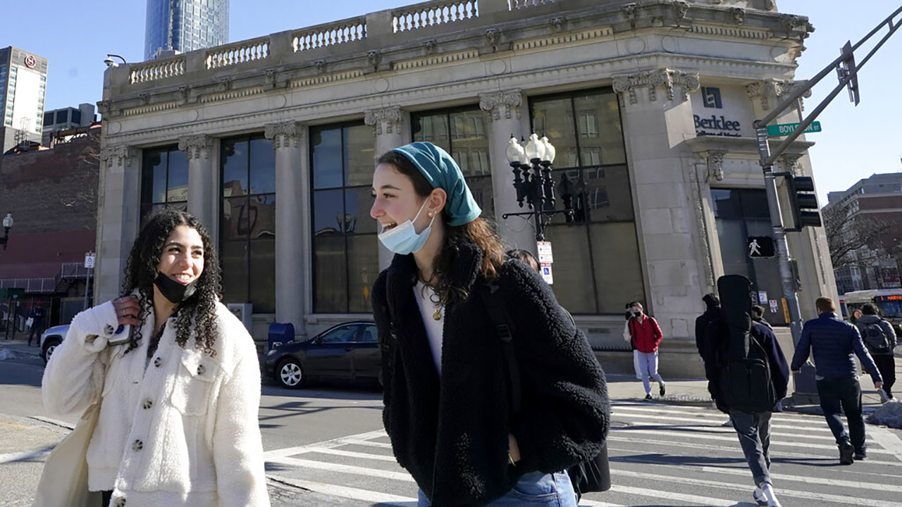 Passers-by wear masks under their chins as they chat with one another while crossing a street, in Boston, Wednesday, Feb. 9, 2022. (AP Photo/Steven Senne, File)