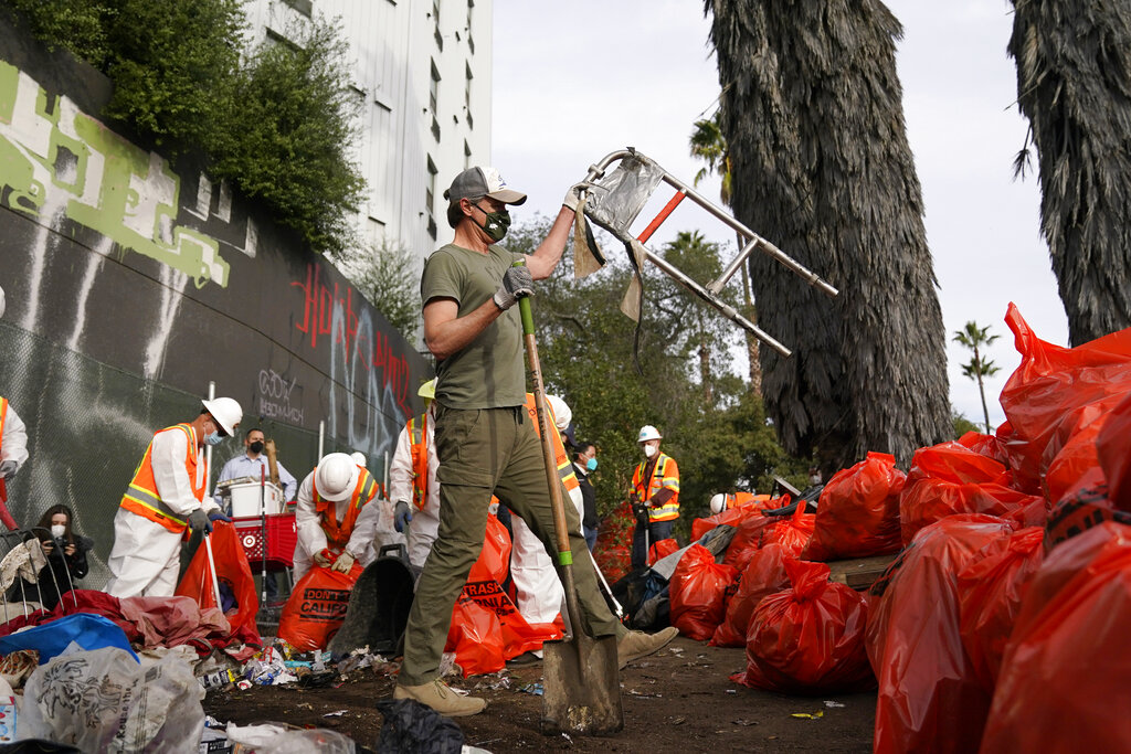 California Gov. Gavin Newsom, center, helps clean a homeless encampment alongside a freeway on Jan. 12, 2022, in San Diego. California's governor proposed a plan on Thursday, March 3, 2022, to force homeless people with severe mental health and addiction disorders into treatment. (AP Photo/Gregory Bull, File)