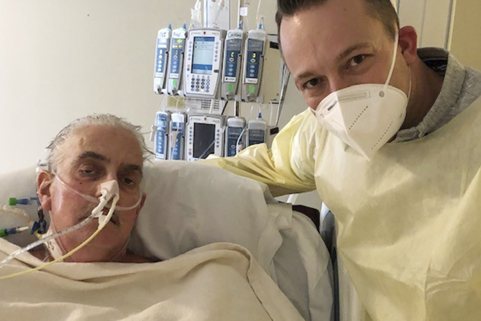 In this photo provided by the University of Maryland School of Medicine, David Bennett Jr., right, stands next to his father's hospital bed in Baltimore, Md., on Jan. 12, 2022, five days after doctors transplanted a pig heart into Bennett Sr., in a last-ditch effort to save his life. Bennett, the first person to receive a heart transplant from a pig died Tuesday, March 8, at the University of Maryland Medical Center, two months after the groundbreaking experiment. His death was announced Wednesday.(University of Maryland School of Medicine via AP)