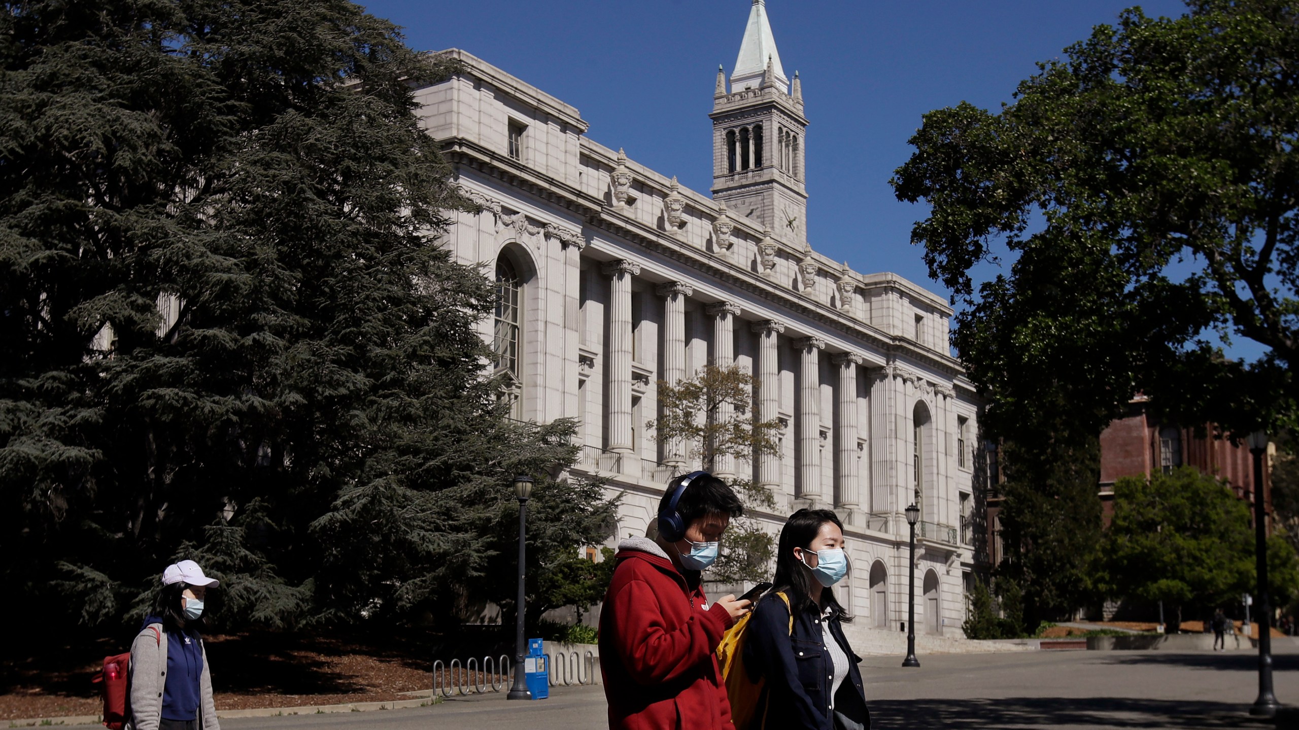 In this March 11, 2020 photo, people wear masks while walking past Wheeler Hall on the University of California campus in Berkeley, Calif. (AP Photo/Jeff Chiu, File)