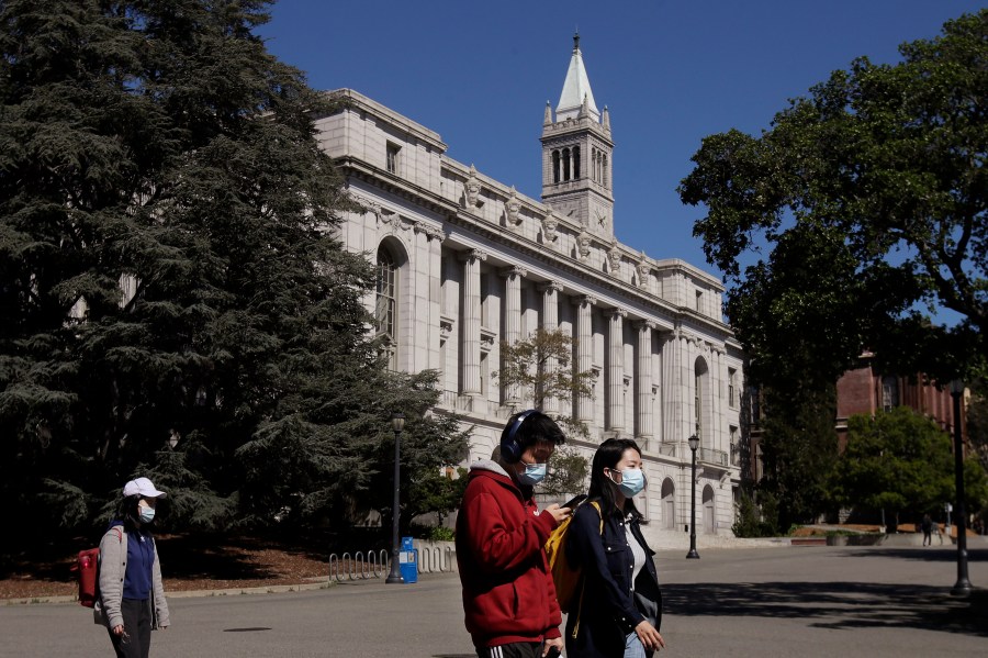 In this March 11, 2020 photo, people wear masks while walking past Wheeler Hall on the University of California campus in Berkeley, Calif. (AP Photo/Jeff Chiu, File)