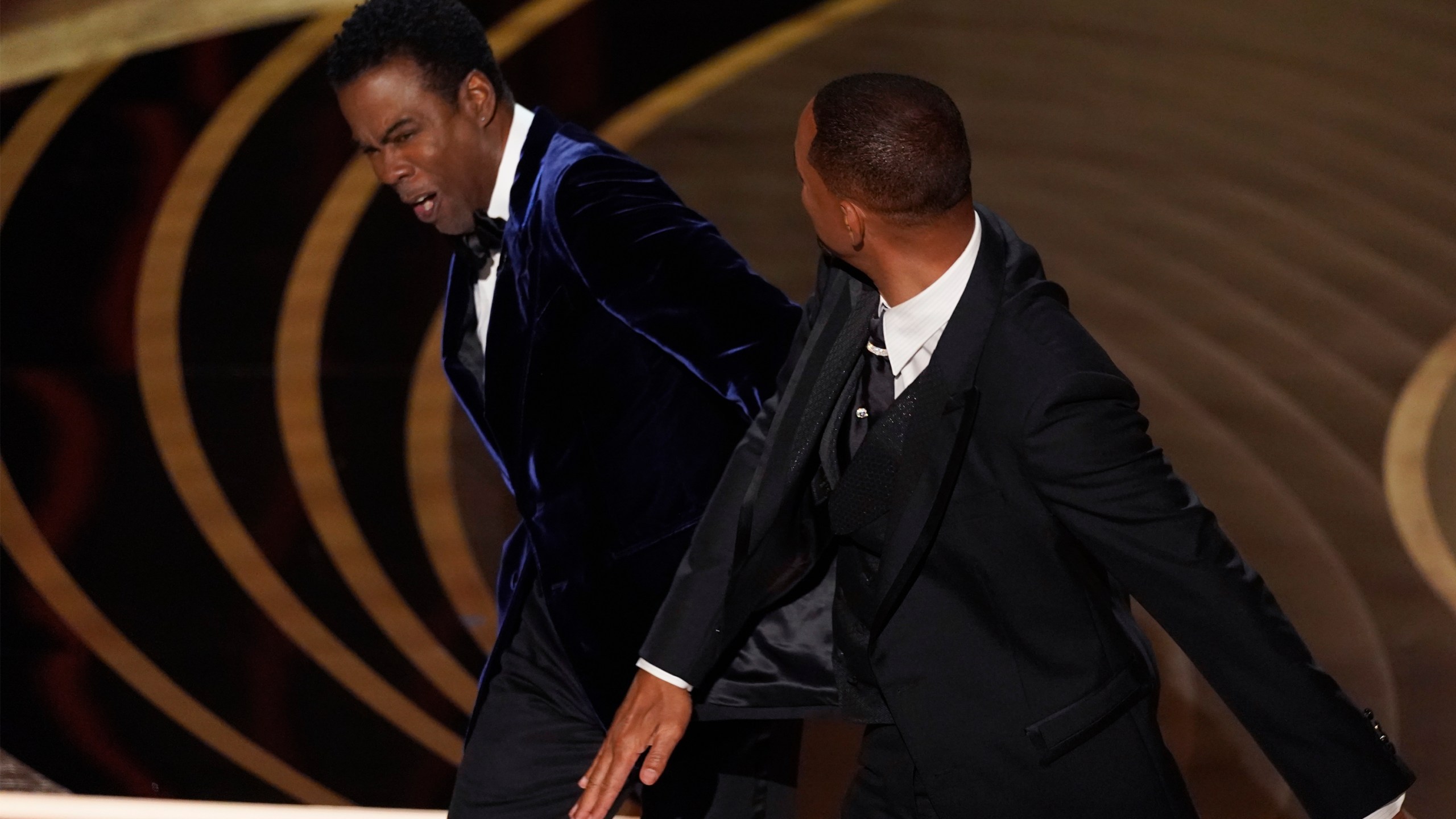 Will Smith, right, hits presenter Chris Rock on stage while presenting the award for best documentary feature at the Oscars on Sunday, March 27, 2022, at the Dolby Theatre in Los Angeles. (AP Photo/Chris Pizzello)