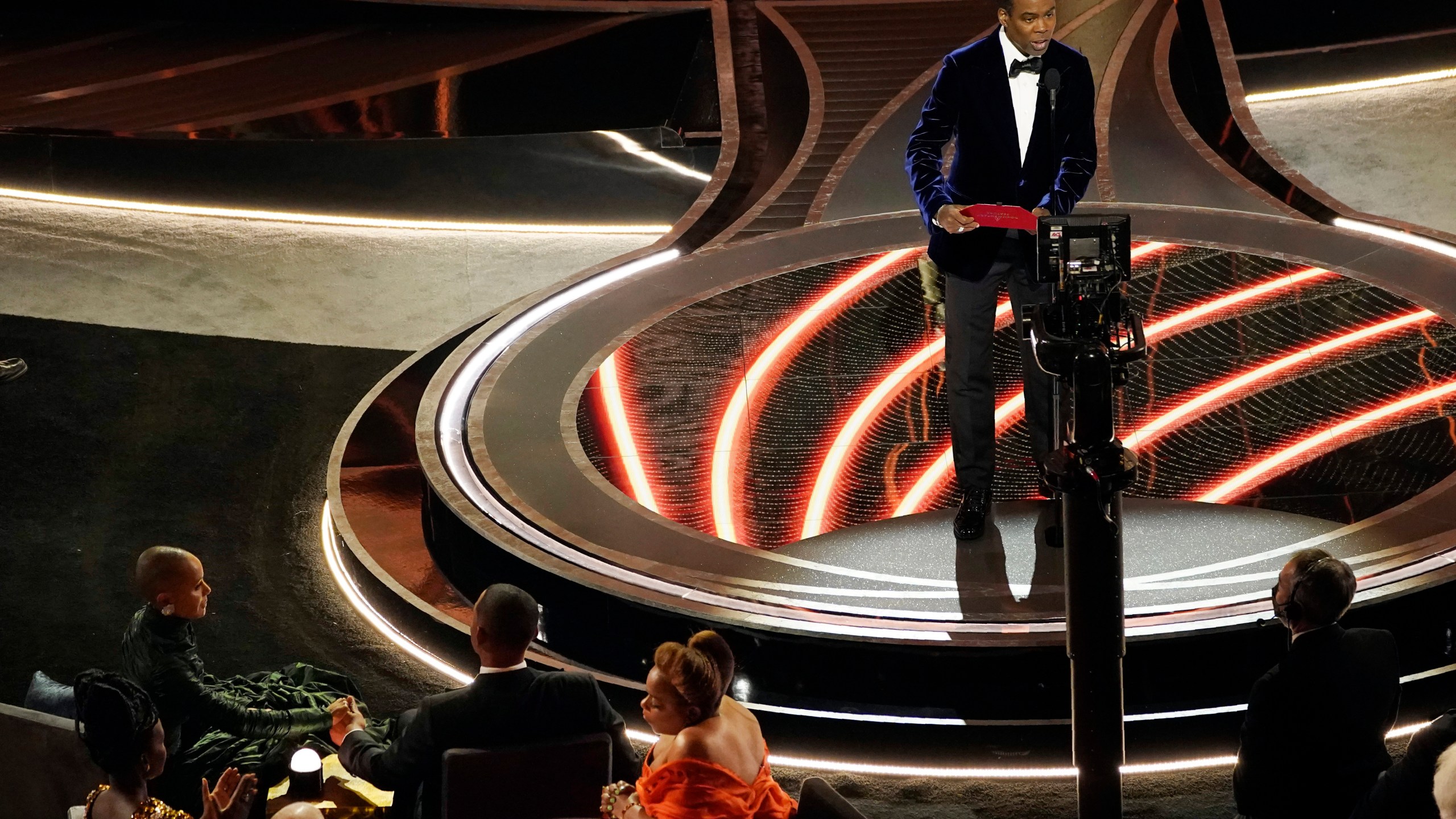 Presenter Chris Rock, right, speaks onstage as Jada Pinkett Smith and Will Smith, bottom left, look on after Smith went onstage and slapped Rock at the Oscars on March 27, 2022, at the Dolby Theatre in Los Angeles. (AP Photo/Chris Pizzello)