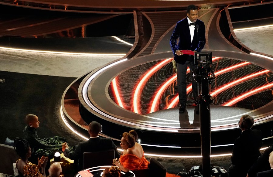 Presenter Chris Rock, right, speaks onstage as Jada Pinkett Smith and Will Smith, bottom left, look on after Smith went onstage and slapped Rock at the Oscars on March 27, 2022, at the Dolby Theatre in Los Angeles. (AP Photo/Chris Pizzello)