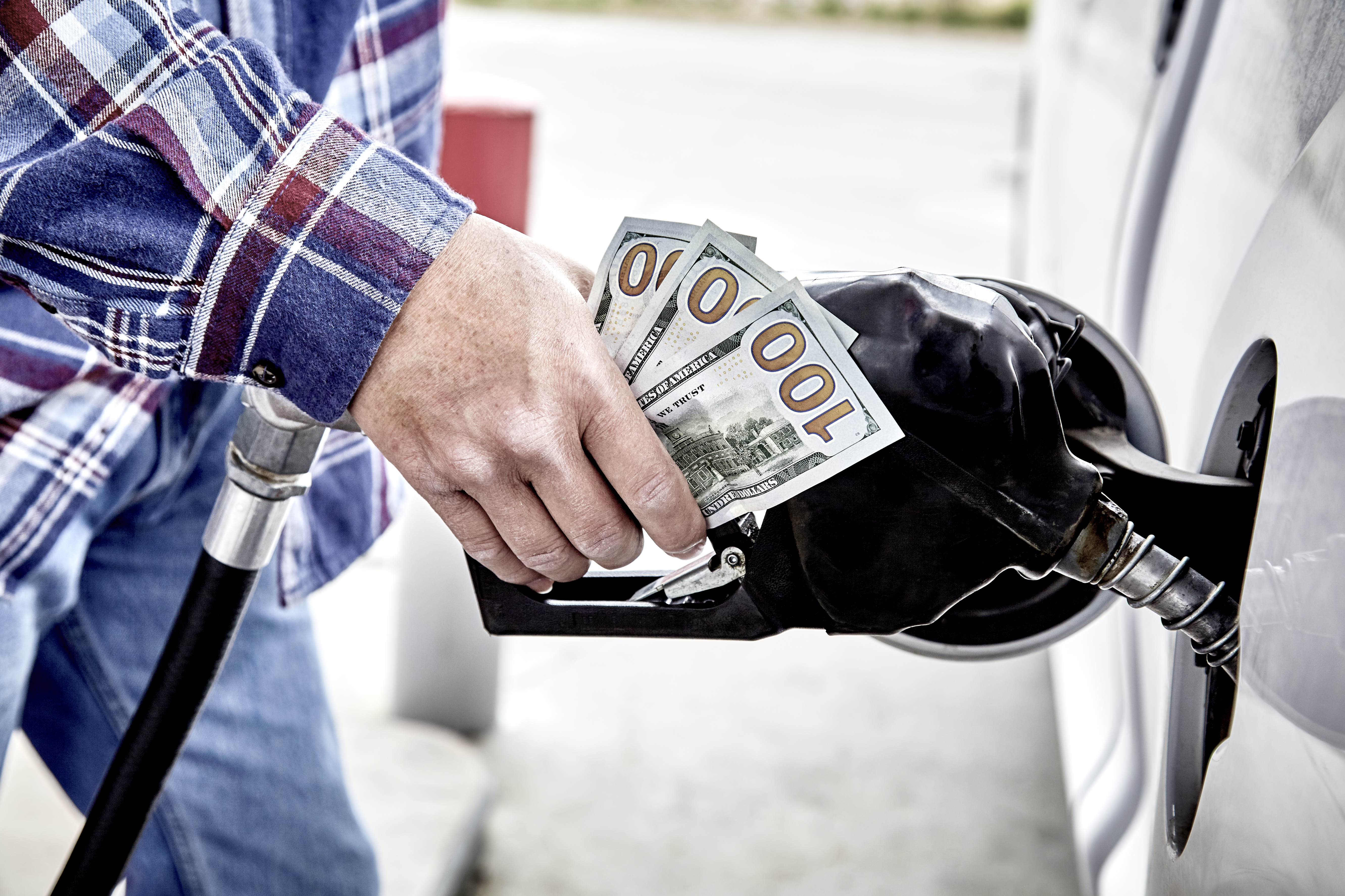 A man holds hundred dollar bills while pumping gas in this undated file photo. (Getty Images)