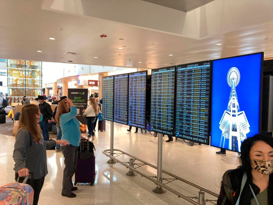 Travelers at Seattle-Tacoma International Airport check the status of flights, including a few that were canceled, on displays inside a gate terminal on April 1, 2022, in Seattle. (AP Photo/Ted S. Warren)