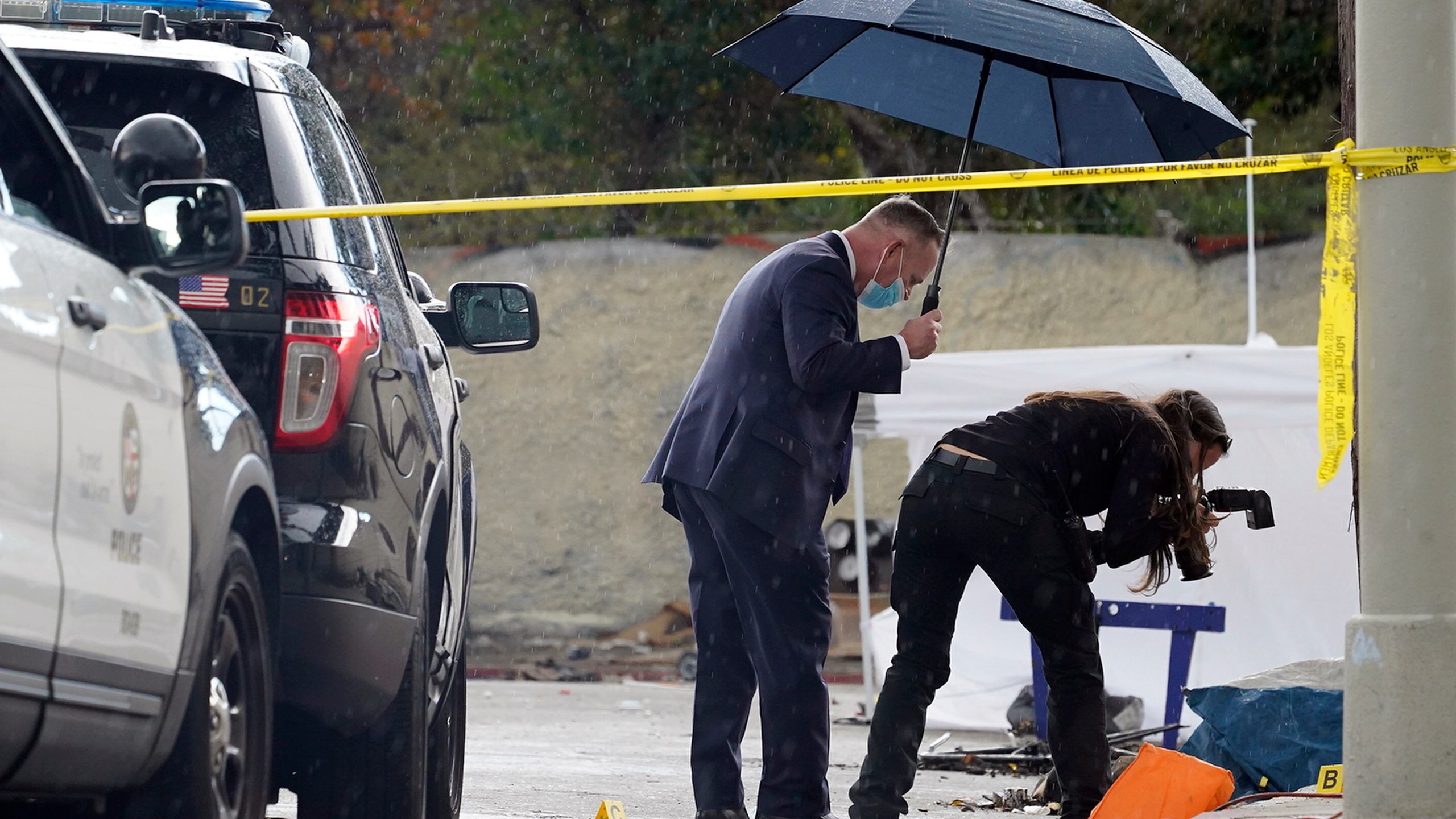 A Los Angeles Police investigator takes pictures in the rain, as investigators gather evidence in the death of an adult male found dead at a homeless encampment in downtown Los Angeles on March 12, 2021. A new report shows that nearly 2,000 homeless people died in Los Angeles County during the first year of the pandemic, an increase of 56% from the previous year, driven mainly by drug overdoses. The findings released Friday, April 22, 2022, in a report from the county's Department of Public Health are the latest illustration of how the COVID-19 pandemic impacted California's staggering population of unhoused people. (AP Photo/Damian Dovarganes, File)