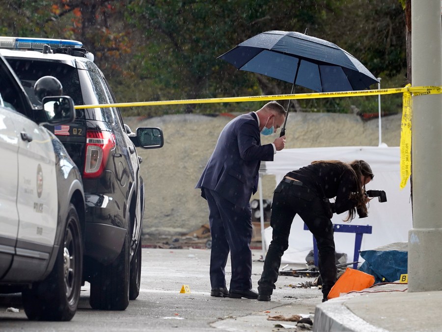 A Los Angeles Police investigator takes pictures in the rain, as investigators gather evidence in the death of an adult male found dead at a homeless encampment in downtown Los Angeles on March 12, 2021. A new report shows that nearly 2,000 homeless people died in Los Angeles County during the first year of the pandemic, an increase of 56% from the previous year, driven mainly by drug overdoses. The findings released Friday, April 22, 2022, in a report from the county's Department of Public Health are the latest illustration of how the COVID-19 pandemic impacted California's staggering population of unhoused people. (AP Photo/Damian Dovarganes, File)