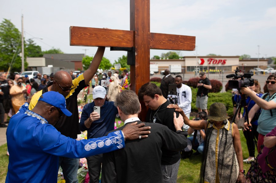 A group prays at the site of a memorial for the victims of the Buffalo supermarket shooting outside the Tops Friendly Market on Saturday, May 21, 2022, in Buffalo, N.Y. Tops was encouraging people to join its stores in a moment of silence to honor the shooting victims Saturday at 2:30 p.m., the approximate time of the attack a week earlier. Buffalo Mayor Byron Brown also called for 123 seconds of silence from 2:28 p.m. to 2:31 p.m., followed by the ringing of church bells 13 times throughout the city to honor the 10 people killed and three wounded. (AP Photo/Joshua Bessex)