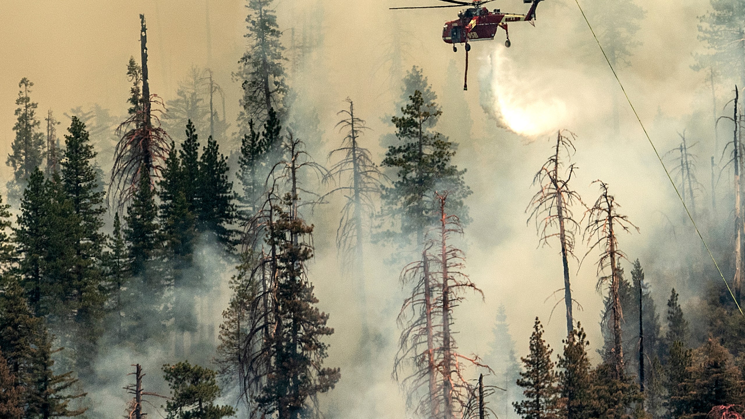 Seen from unincorporated Mariposa County, Calif., a helicopter drops water on the Washburn Fire burning in Yosemite National Park, Saturday, July 9, 2022. (AP Photo/Noah Berger)