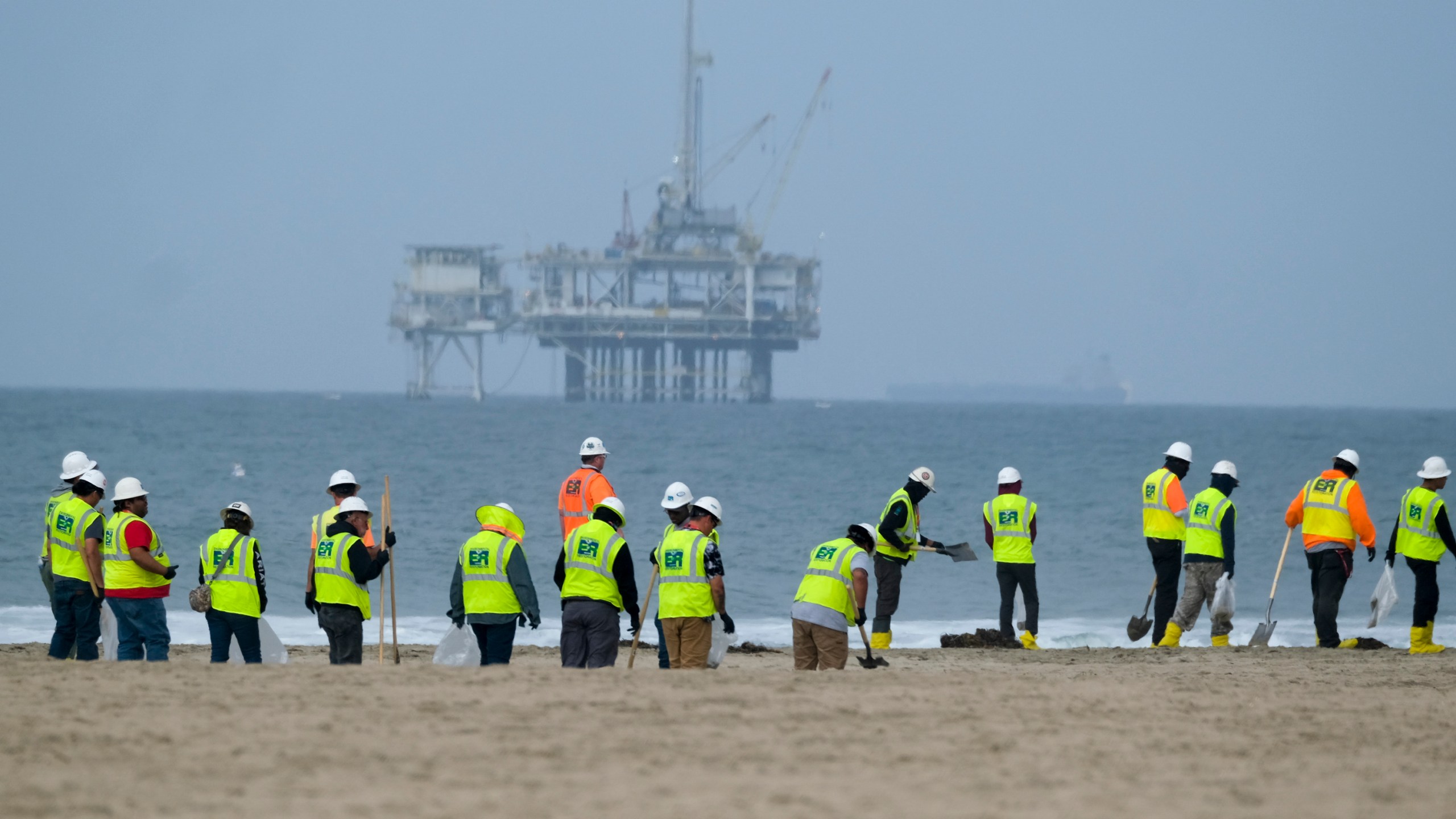 Workers in protective suits continue to clean the contaminated beach with a platform in the background in Huntington Beach, Calif., on Oct. 11, 2021. A pipeline operator and two subsidiaries have agreed to plead guilty to negligently discharging oil off the Southern California coast in connection with a pipeline break that covered beaches with blobs of crude. (AP Photo/Ringo H.W. Chiu, File)