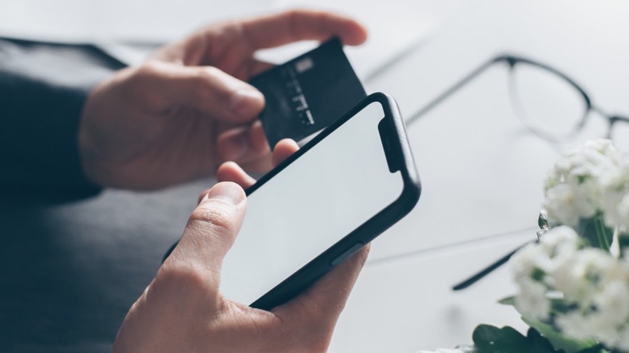 A man holds a credit card and a cell phone in this undated editorial image. (Photo by Mikhail Nilov/Pexels)