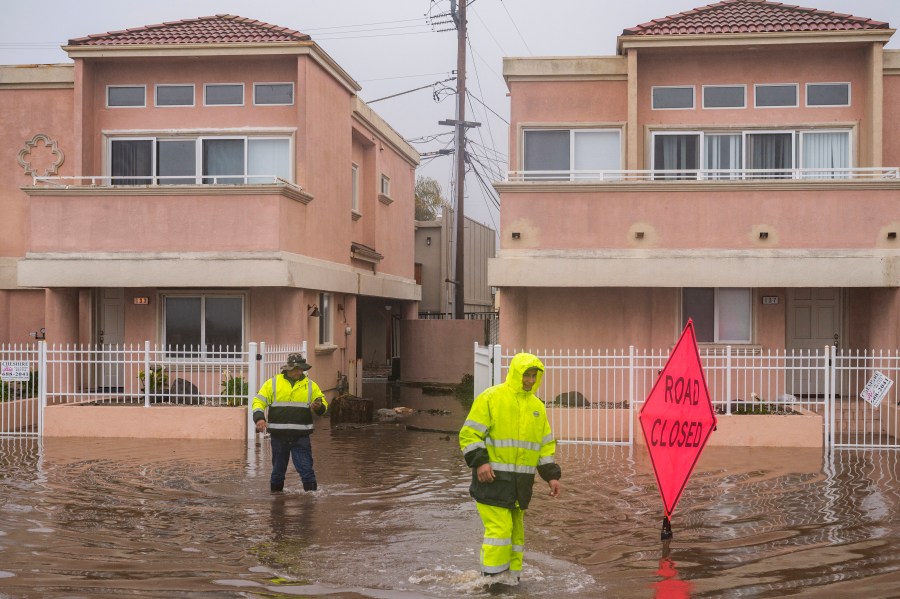 A cleaning crew walks through floodwaters in the Rio Del Mar neighborhood of Aptos, Calif. on Jan. 9, 2023. (Nic Coury/Associated Press)