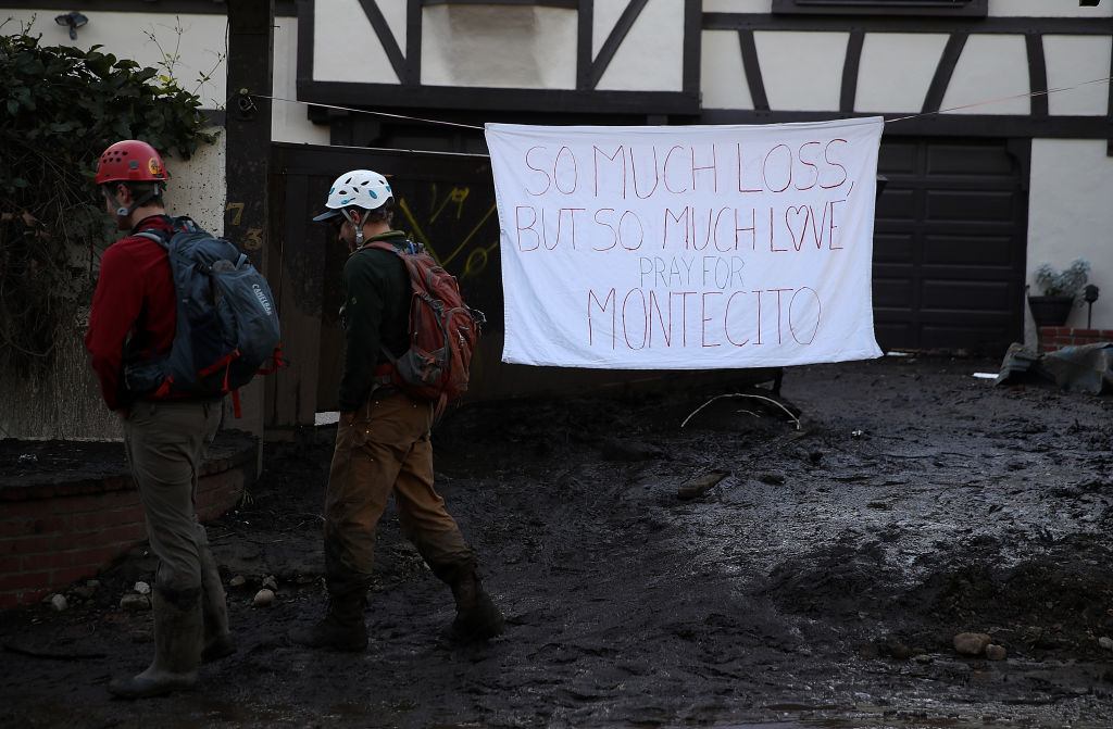 People walk by a homemade sign that hangs in front of a home after a mudslide on January 10, 2018 in Montecito, California. 17 people have died and hundreds hundreds of homes have been destroyed or damaged after massive mudslides crashed through Montecito, California early Tuesday morning. (Photo by Justin Sullivan/Getty Images)