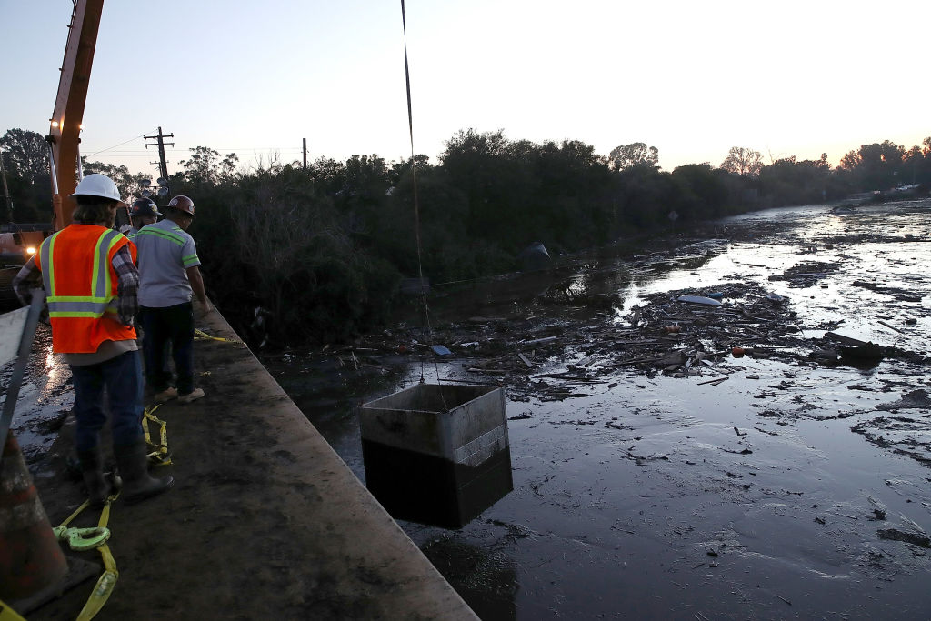 Workers drop a box that will house pumps in a flooded section of Highway 101 on January 11, 2018 in Montecito, California. 17 people have died and hundreds of homes have been destroyed or damaged after massive mudslides crashed through Montecito, California early Tuesday morning. (Photo by Justin Sullivan/Getty Images)