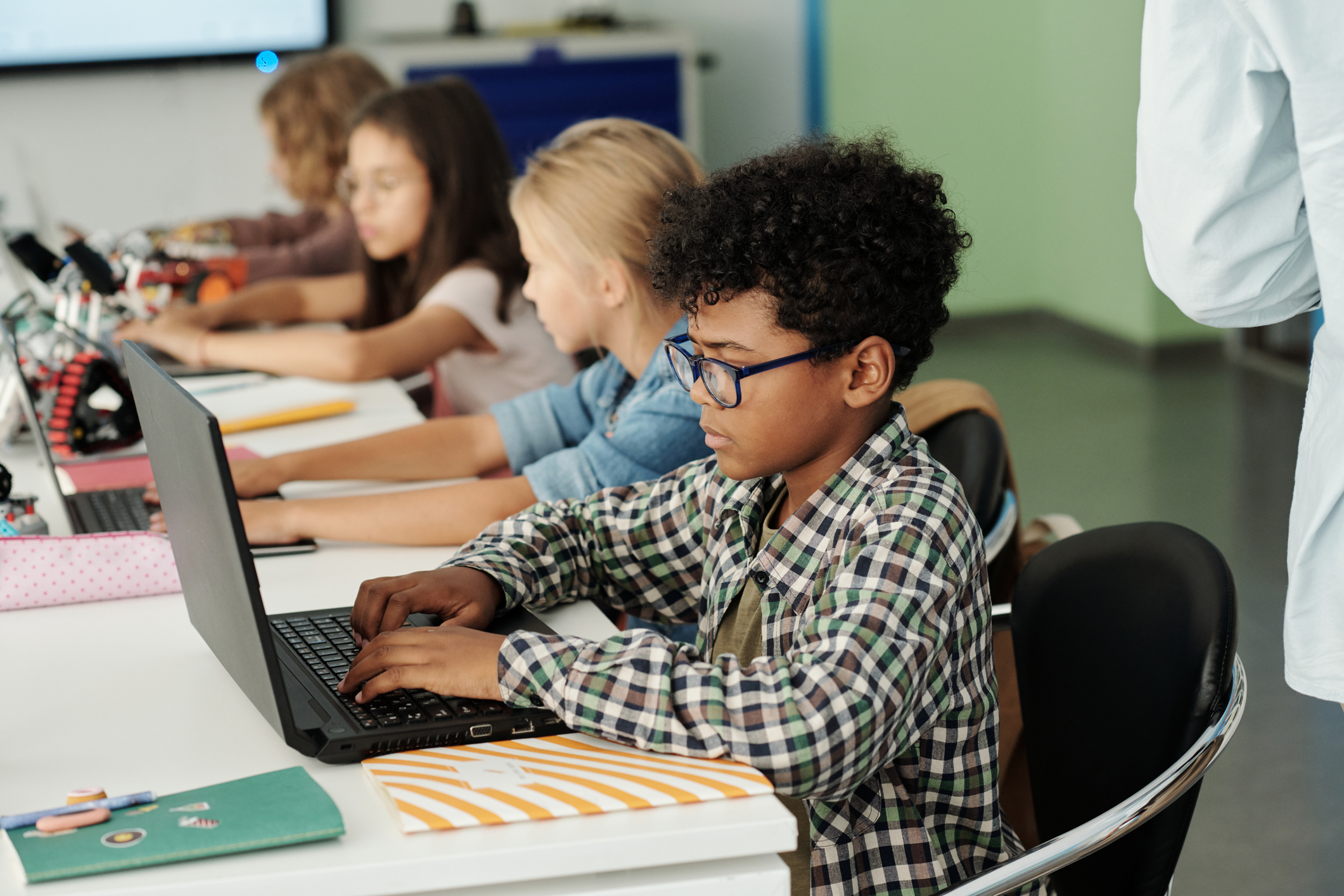 School children working in front of laptops while sitting in row by desk