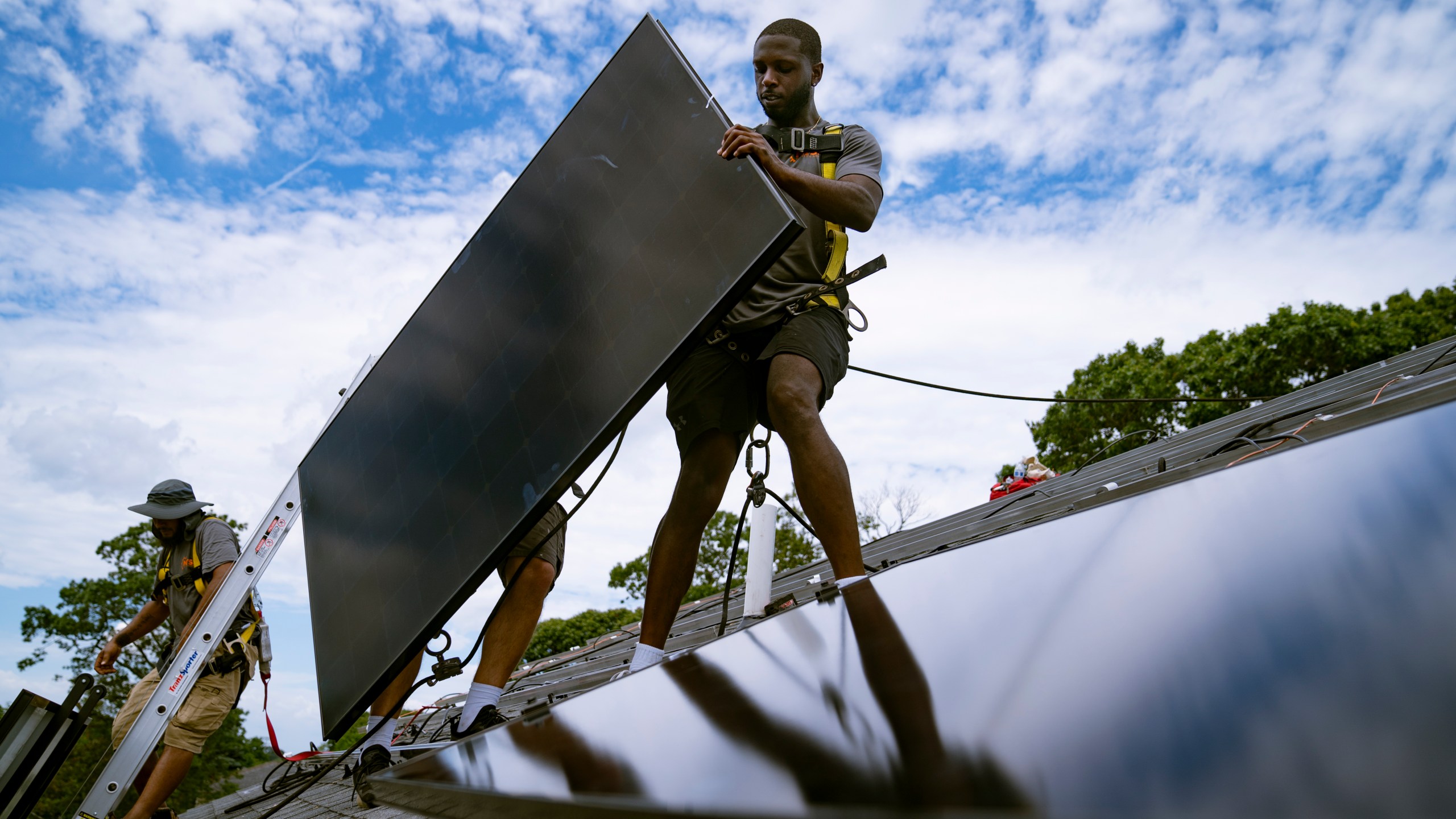 FILE - Employees of NY State Solar, a residential and commercial photovoltaic systems company, install an array of solar panels on a roof, Aug. 11, 2022, in the Long Island hamlet of Massapequa, N.Y. The Biden administration is announcing Thursday, April 20, 2023, more than $80 million in funding as part of a push to make more solar panels in the U.S. and make solar energy available in more communities. (AP Photo/John Minchillo, File)