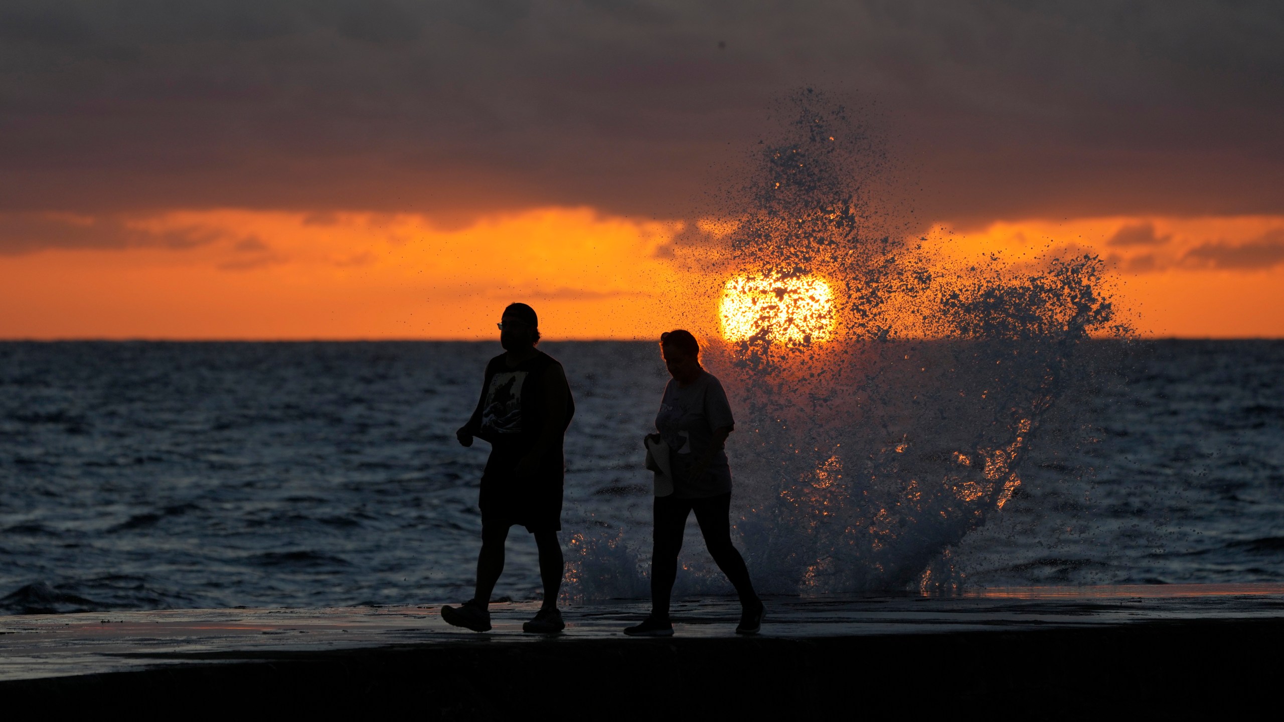 FILE - The sun rises above the Atlantic Ocean as waves crash near beach goers walking along a jetty, Dec. 7, 2022, in Bal Harbour, Fla. The world's oceans have suddenly spiked much hotter and well above record levels, with scientists trying to figure out what it means and whether it forecasts a surge in atmospheric warming. (AP Photo/Wilfredo Lee, File)