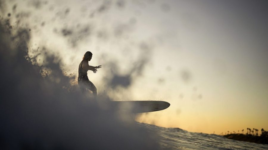 A woman surfs a longboard as the sun sets on a hot day.