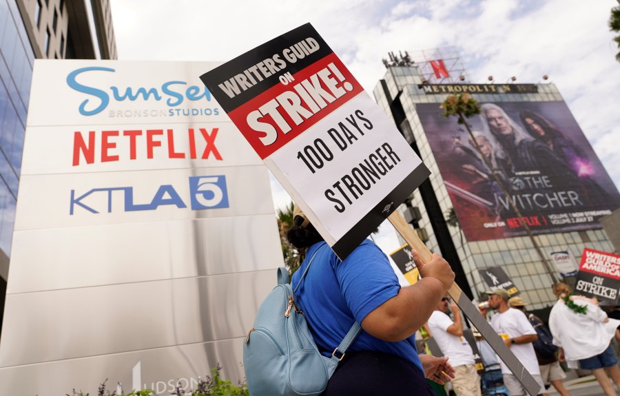 A picketer carries a sign outside Netflix studios on Wednesday, Aug. 9, 2023, in Los Angeles. The Hollywood writers strike reached the 100-day mark today as the U.S. film and television industries remain paralyzed by dual actors and screenwriters strikes. (AP Photo/Chris Pizzello)