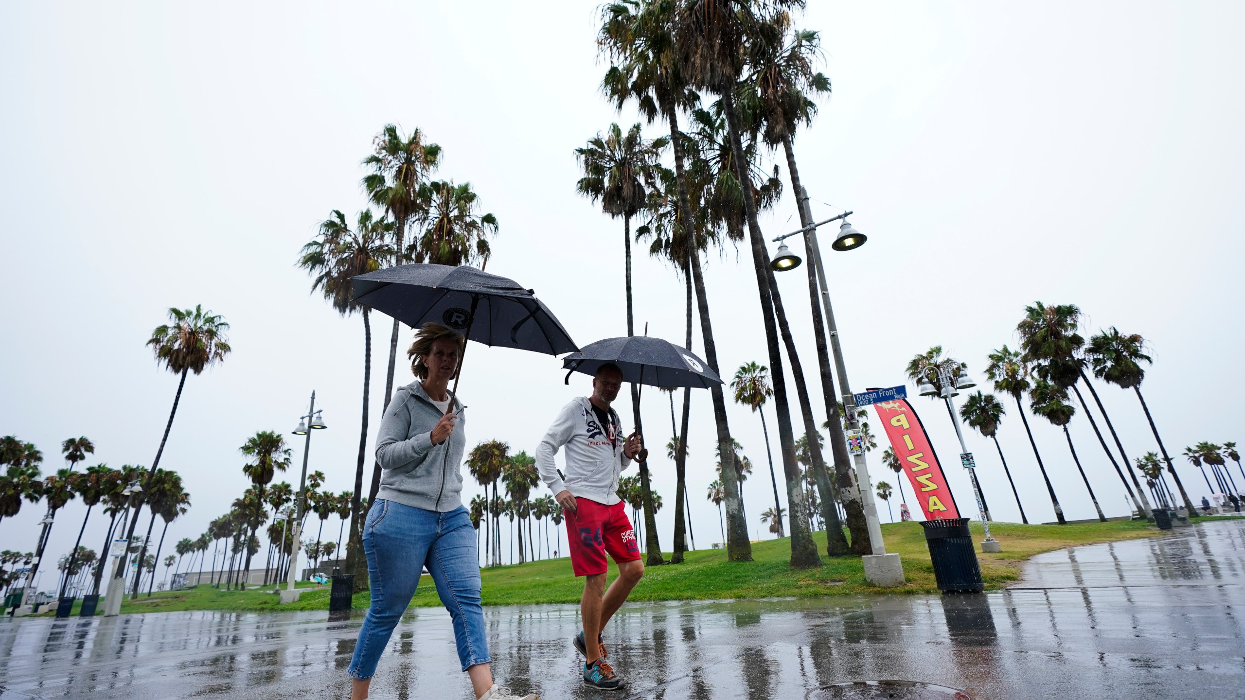 People walk along Venice Beach in the rain, Sunday, Aug. 20, 2023, in Los Angeles. Tropical Storm Hilary swirled northward Sunday just off the coast of Mexico's Baja California peninsula, no longer a hurricane but still carrying so much rain that forecasters said "catastrophic and life-threatening" flooding is likely across a broad region of the southwestern U.S. (AP Photo/Ryan Sun)