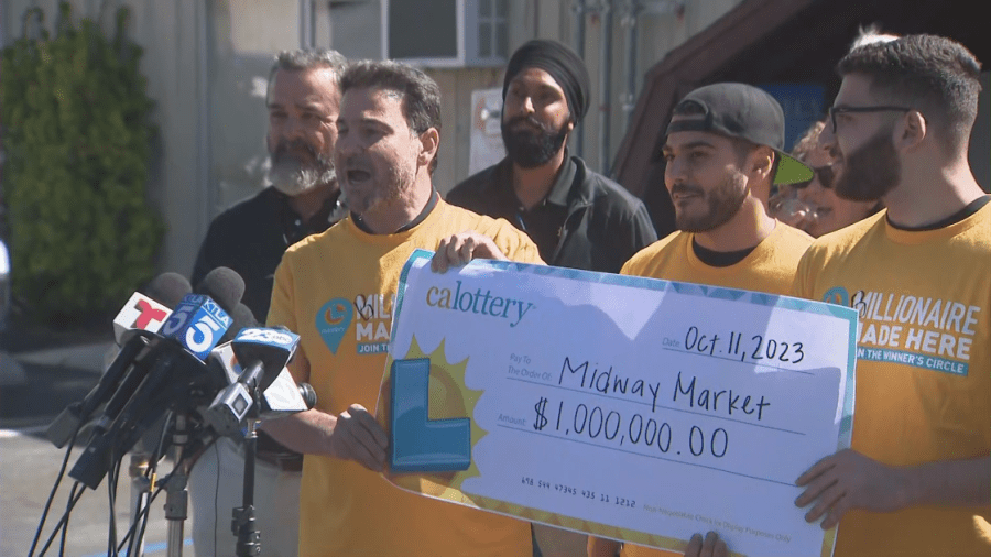 Owner Andy Khalil (left) holds a check for $1 million after a winning Powerball ticket was sold at his Midway M