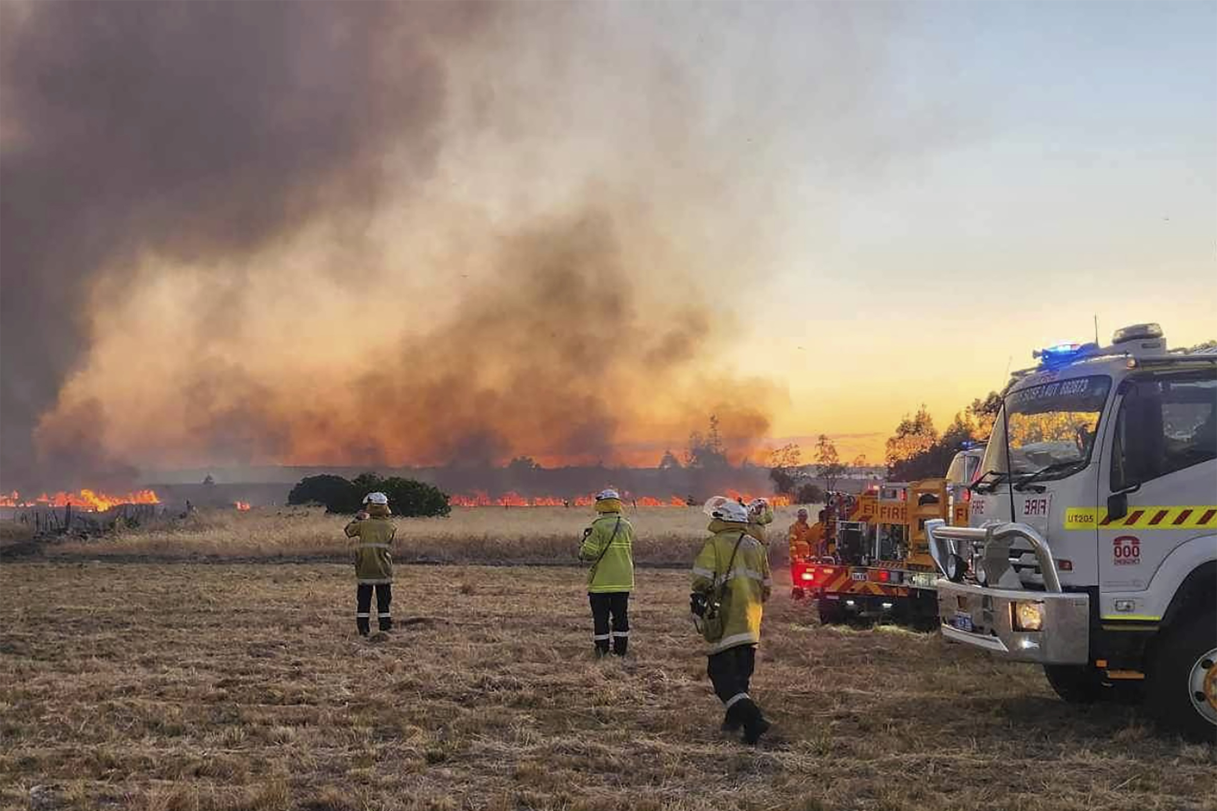 West Australian firefighters watch as grassland burns near the West Australian city of Wannaroo, north of Perth in the early hours of Thursday, Nov. 23, 2023. Dozens of residents have been evacuated and at least 10 homes have been destroyed by a wildfire that is burning out of control on the northern fringe of the west coast city of Perth during heatwave spring conditions, authorities say.(DFES via AP)