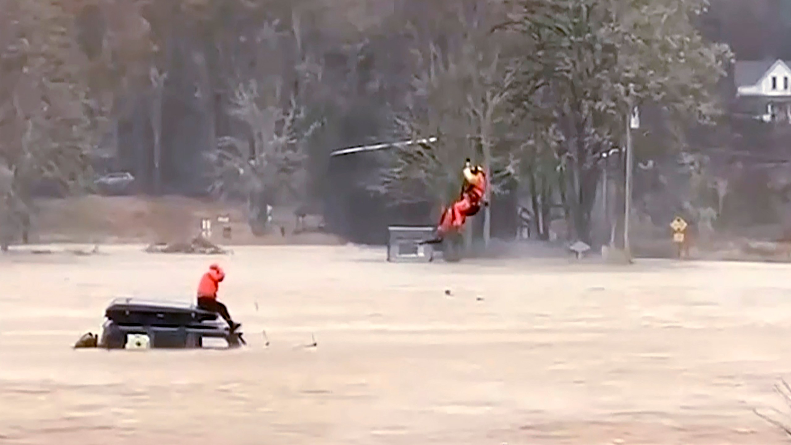 In this still from a video provided by Nicole Langer, a woman is rescued by a U.S. Coast Guard officer from a flooded truck in Grays River, Washington, on Tuesday, Nov. 5, 2023. According to Langer, the woman tried to drive on flooded roads. The Coast Guard aircrew also rescued four other people nearby trapped on top of their house. An atmospheric river brought heavy rain, flooding and unseasonably warm temperatures to the Pacific Northwest. (Nicole Langer via AP)