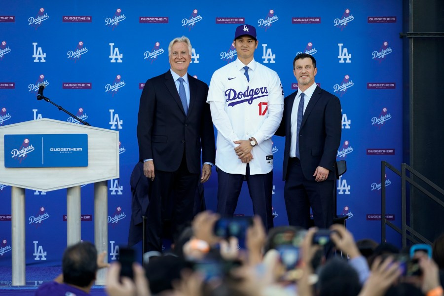 Los Angeles Dodgers' Shohei Ohtani, center, poses for a photo with owner and chairman Mark Walter, left, and president of baseball operations Andrew Friedman applaud during a news conference at Dodger Stadium Thursday, Dec. 14, 2023, in Los Angeles. (AP Photo/Ashley Landis)