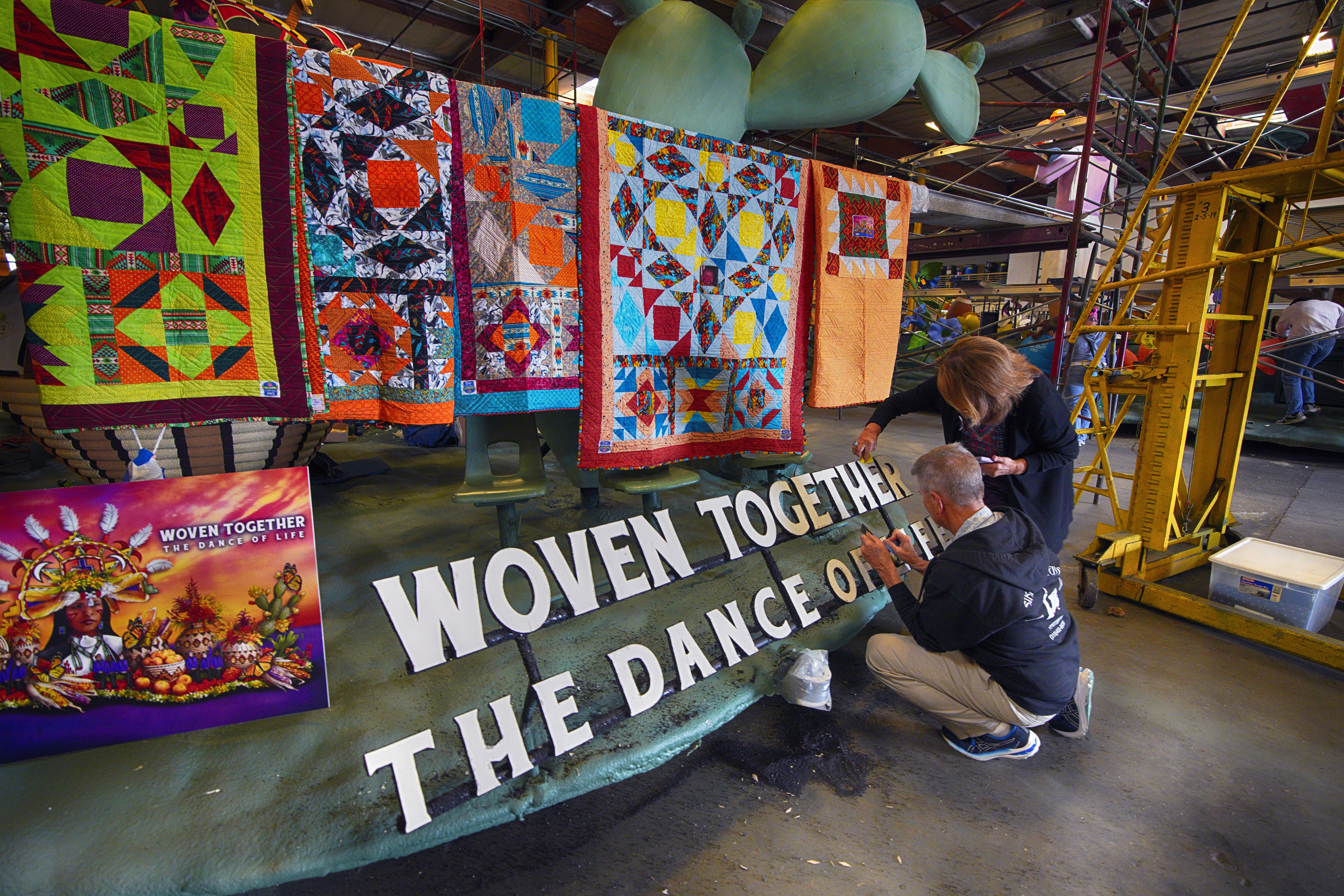 Carrie Holland joined by her husband Jim Holland works on a sign that reads "Woven Together The Dance of Life" on the OneLegacy Donate Life Rose Parade Float in Irwindale, Calif. on Tuesday, Dec. 26, 2023. (AP Photo/Richard Vogel)