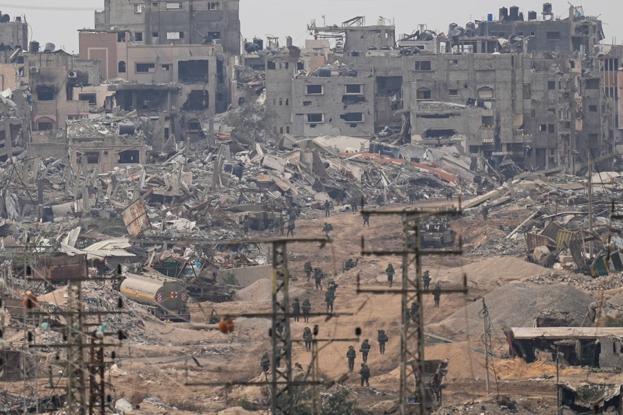 FILE - Israeli troops walk in the Gaza Strip as seen from southern Israel, Dec. 21, 2023. A public school district in Michigan is considering a resolution Wednesday, Jan. 17, 2024, calling for a cease-fire in the Israel-Hamas war while also encouraging its teachers to discuss the conflict in its classrooms. (AP Photo/Ohad Zwigenberg, File)