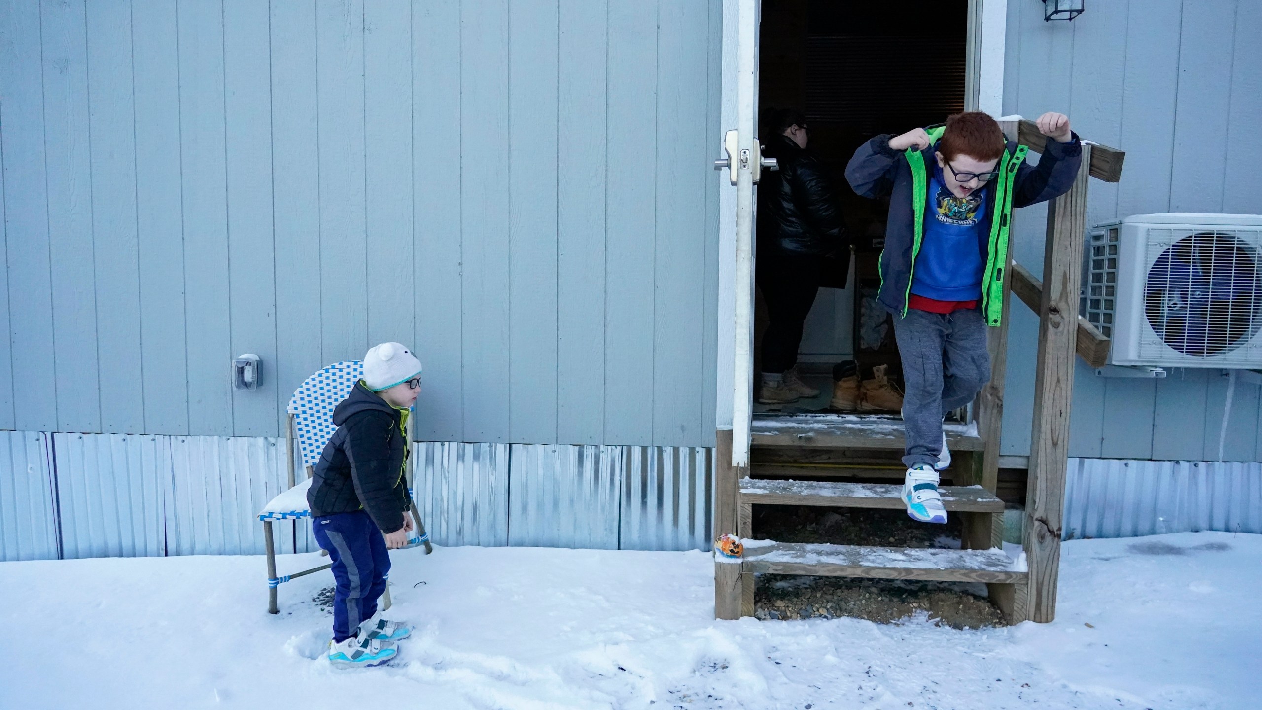 Hunter Prince, right, leaps out of his family's temporary home into the snow as his brother, Waylon, watches, Tuesday, Jan. 16, 2024, in Water Valley, Ky. Two years after the tornado outbreak that killed dozens and leveled much of the real estate in Mayfield, many people, like the Prince family, are still living through another, slower disaster, the search for housing. (AP Photo/Joshua A. Bickel)