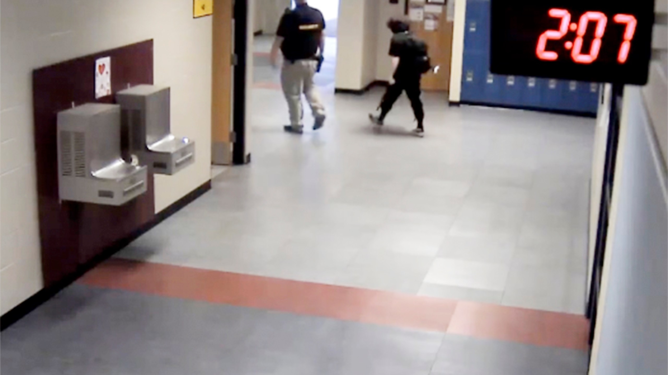 In this image taken from video taken from a school security camera and provided by the Owasso Police Dept., Nex Benedict is seen walking out of the school with a security guard, Feb. 7, 2024, at Owasso High School in Owasso, Okla. A recently released police search warrant is revealing more details in the case of a Benedict, a nonbinary student, who died a day after a high school bathroom fight. (School Security Video/Courtesy of Owasso Police Department via AP)