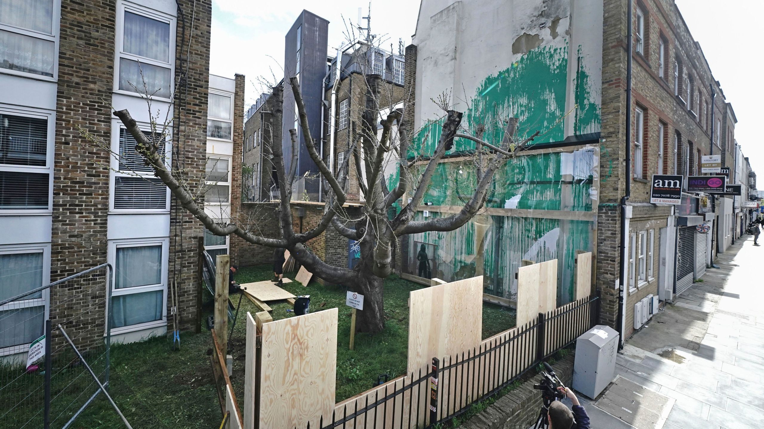 Boarding is put up next to the Banksy artwork on the side of a residential building in Hornsey Road, north London, Wednesday March 27, 2024 which has been covered in perspex sheeting for protection. An environmentally themed mural in London by street artist Banksy has been encased in plastic and surrounded by fencing after an apparent act of vandalism. (Aaron Chown/PA via AP)