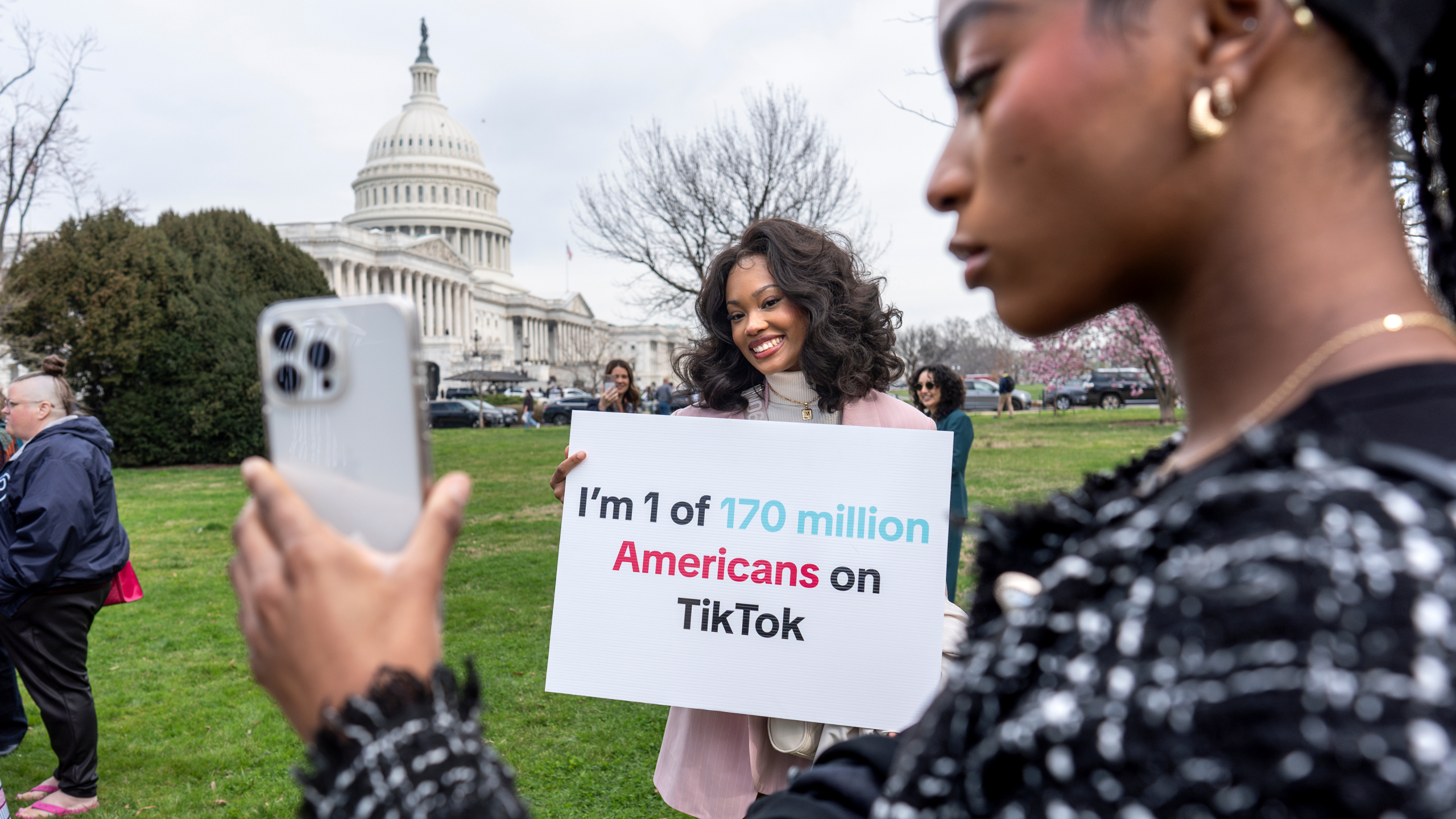 Devotees of TikTok, Mona Swain, center, and her sister, Rachel Swain, right, both of Atlanta, pose with a sign at the Capitol in Washington, March 13, 2024.