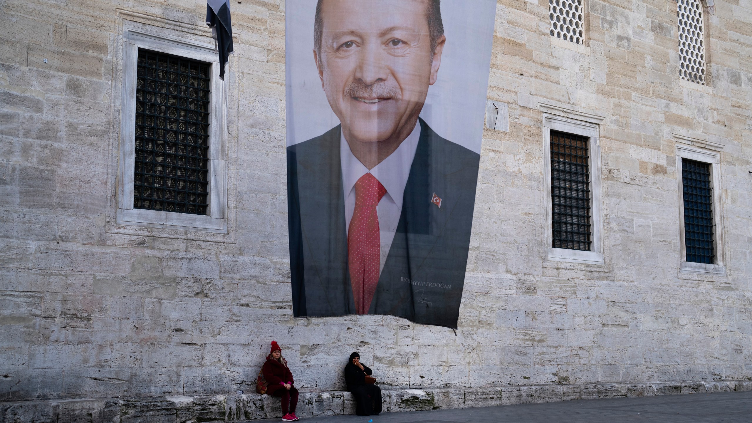 Two women sit near a campaign banner of Turkish President and leader of the Justice and Development Party, or AKP, Recep Tayyip in Istanbul, Turkey, Monday, March 11, 2024. Turkey was coming to terms on Monday with the opposition's unexpected success in local elections which saw it outperform President Recep Tayyip Erdogan's ruling party and add to municipalities gained five years ago. (AP Photo/Francisco Seco)